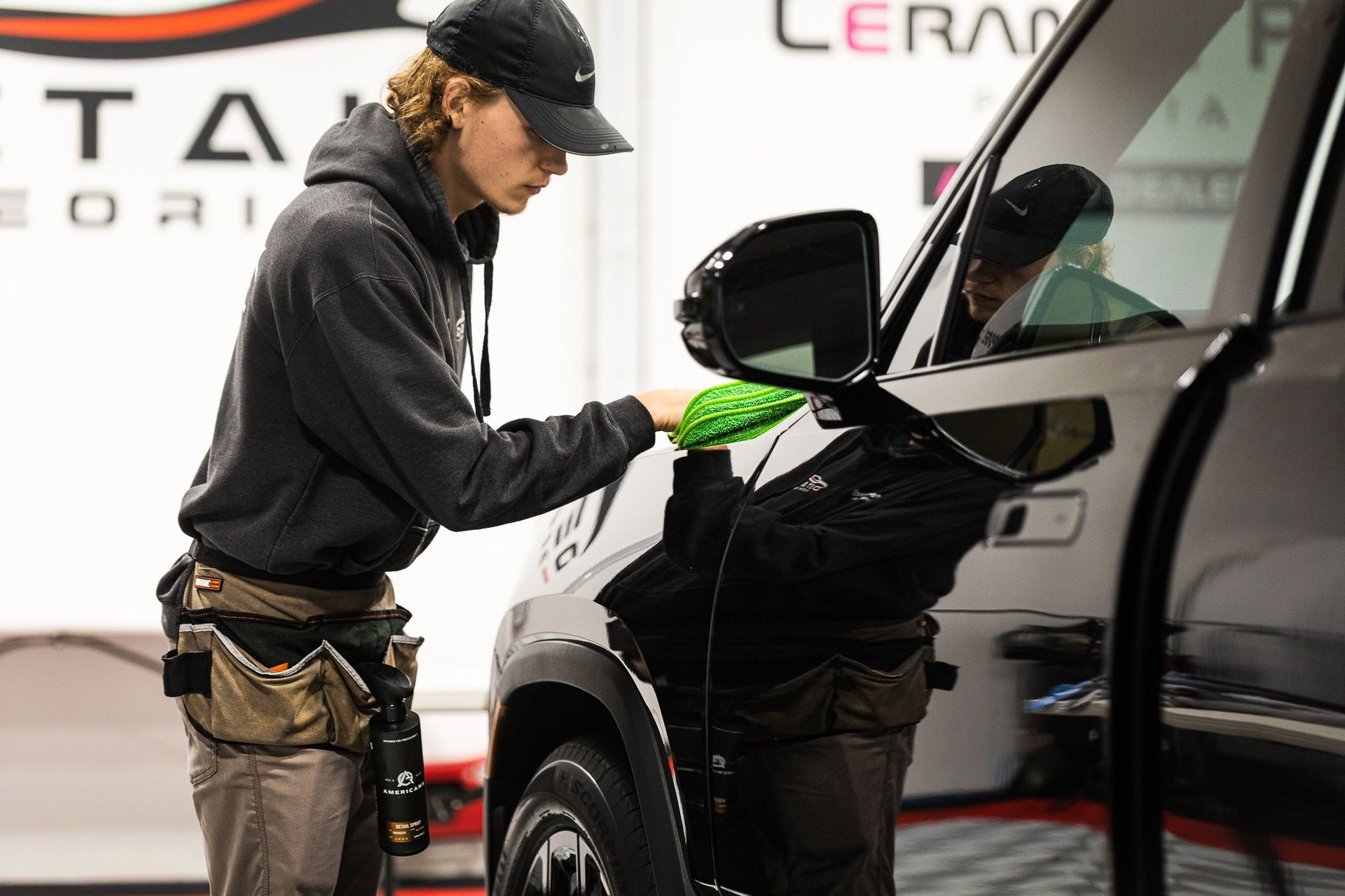 Worker polishing a black car with a green cloth in a garage.