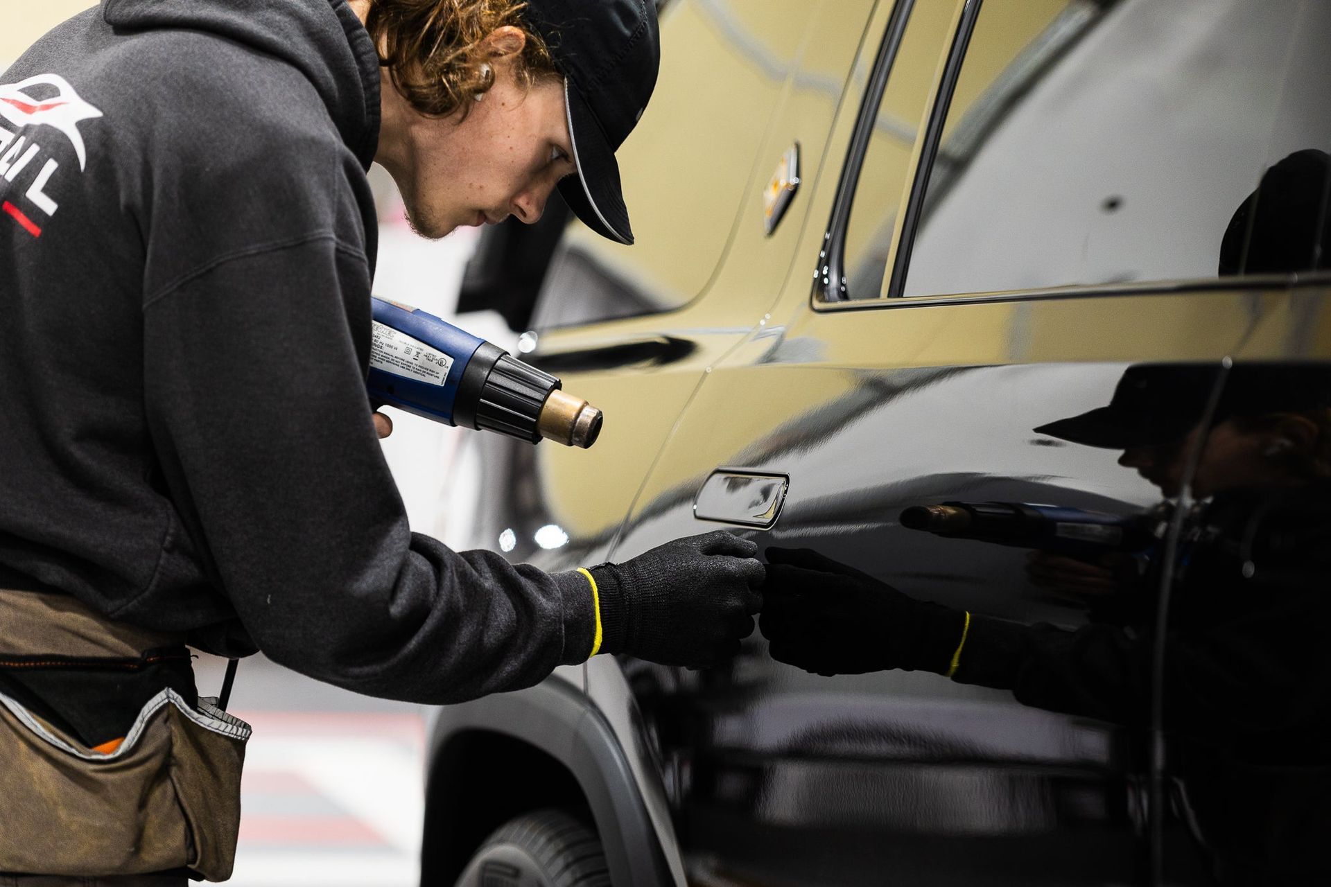 Technician polishing a black car door with a power buffer in a workshop