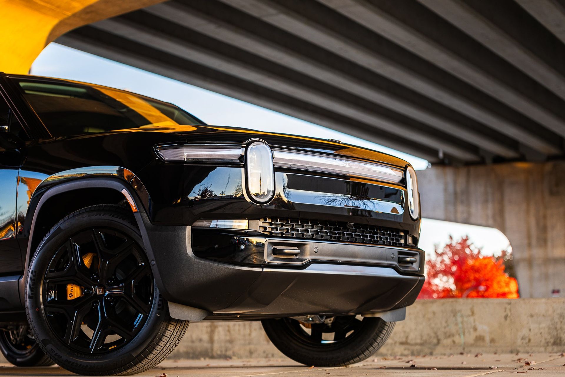 Black pickup truck parked under a concrete overpass with a blurred orange fire in the background