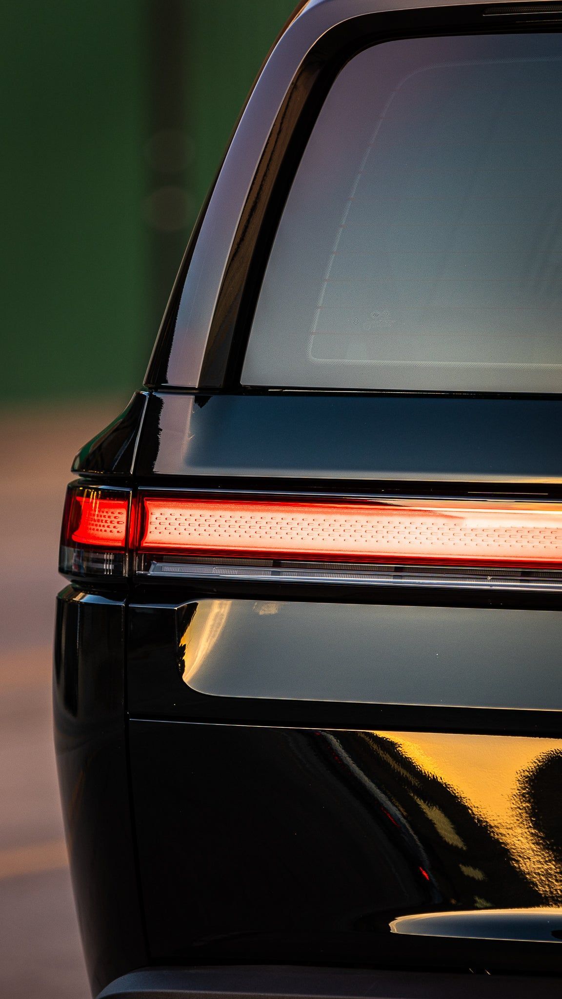 Rear view of a black car with a red taillight and reflective rear window at dusk
