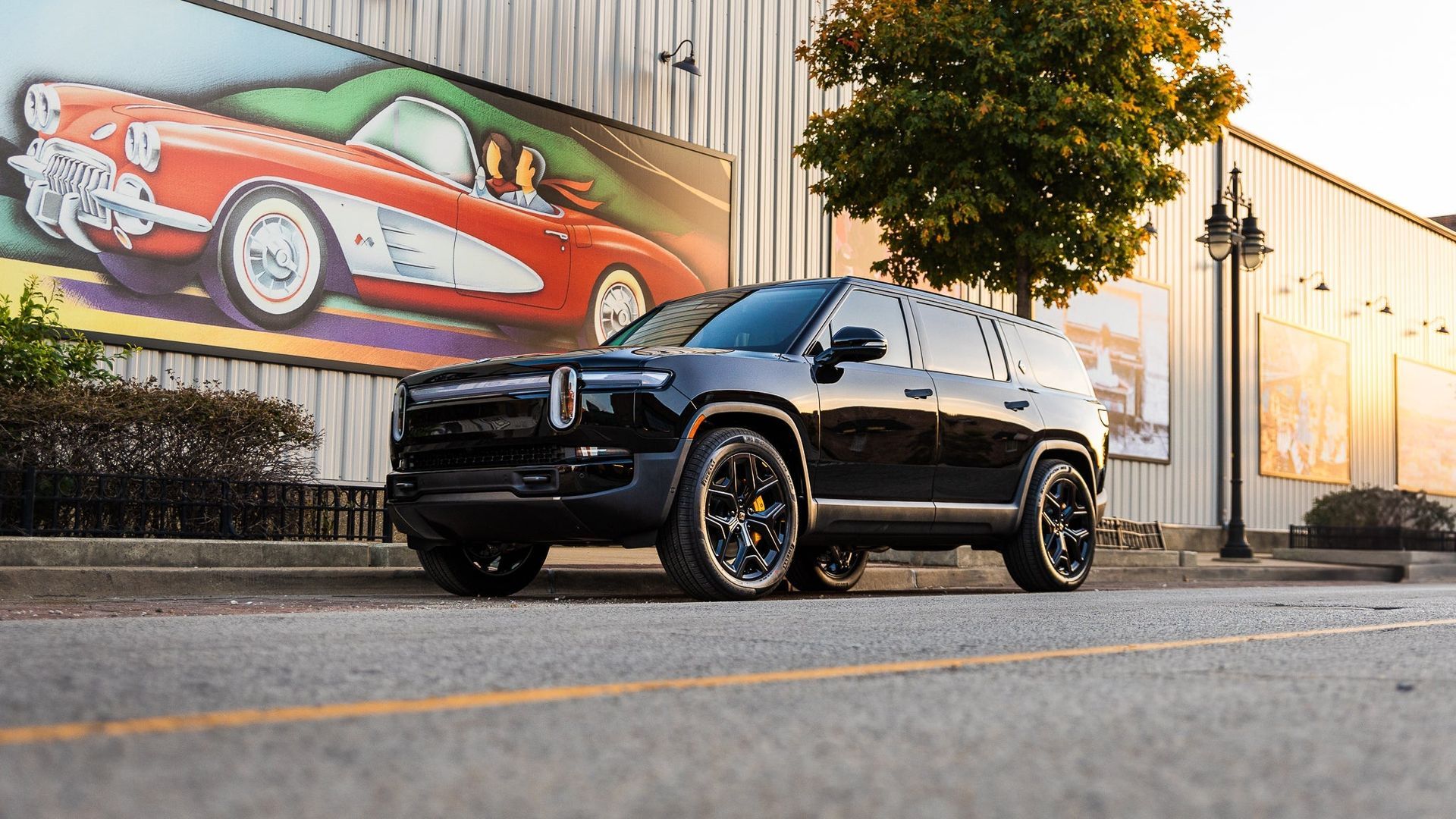 Black SUV parked on a street beside a building with a colorful mural of a red sports car