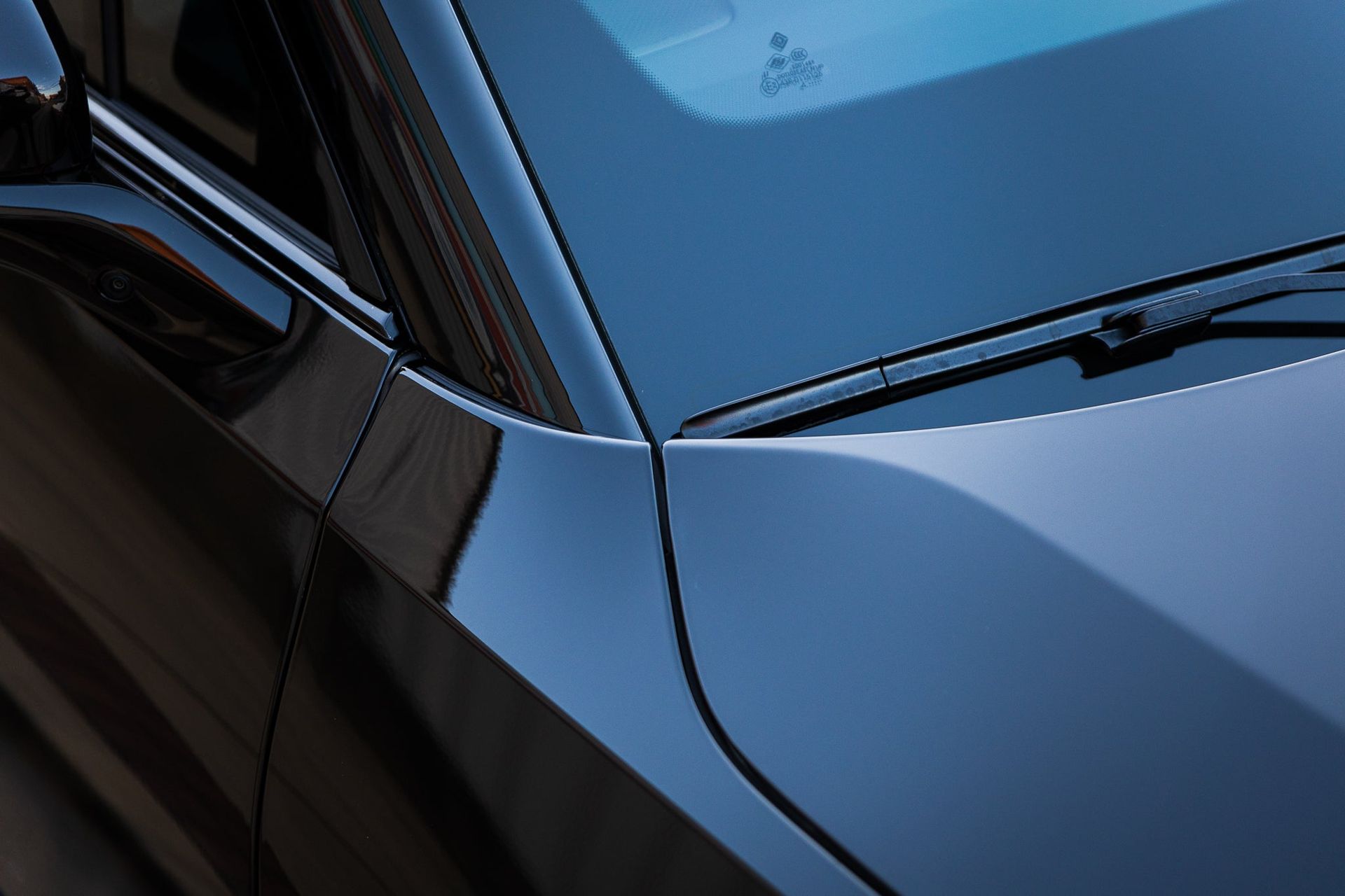 Close-up of a blue car’s side door, window, and windshield with reflections