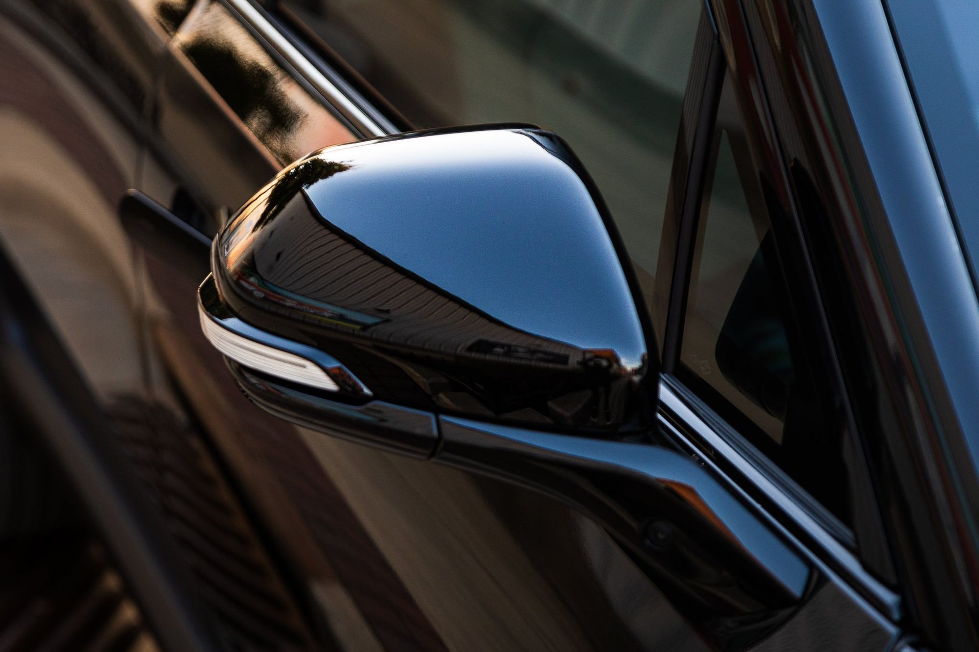 Close-up of a glossy black car side mirror reflecting light