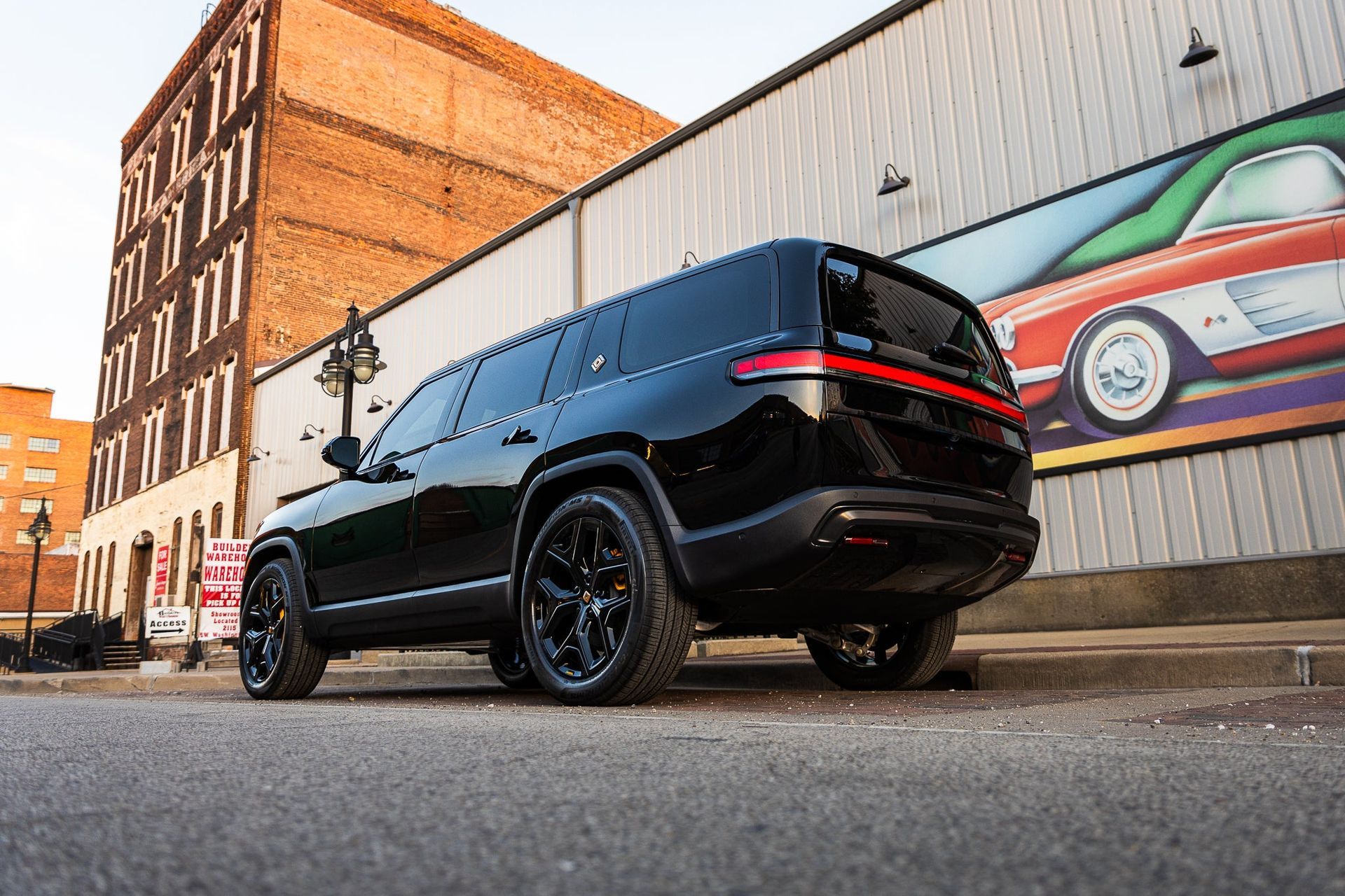 Black SUV parked on a city street beside brick buildings and a mural of a colorful classic car