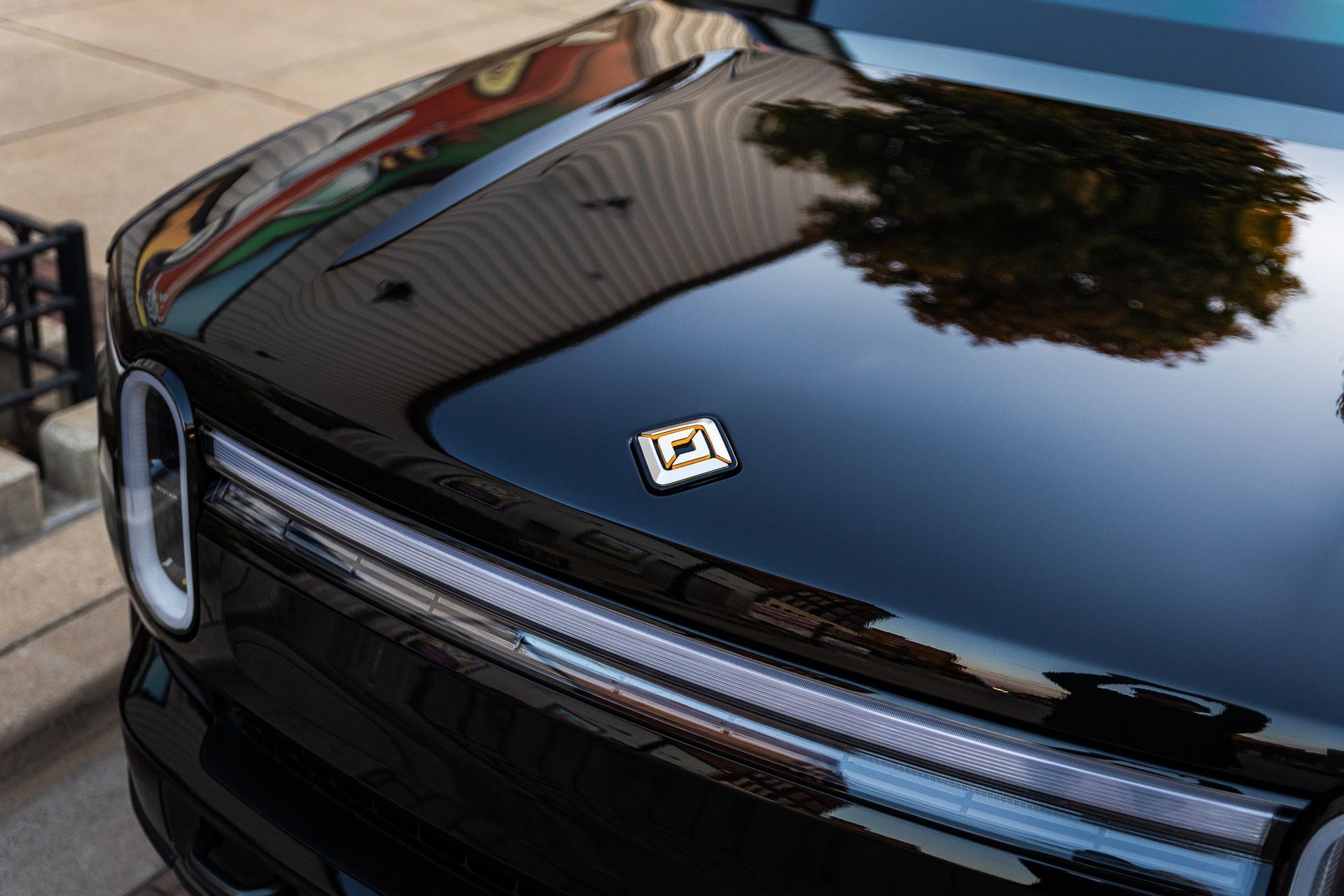 Glossy black car hood with emblem reflecting trees and sky