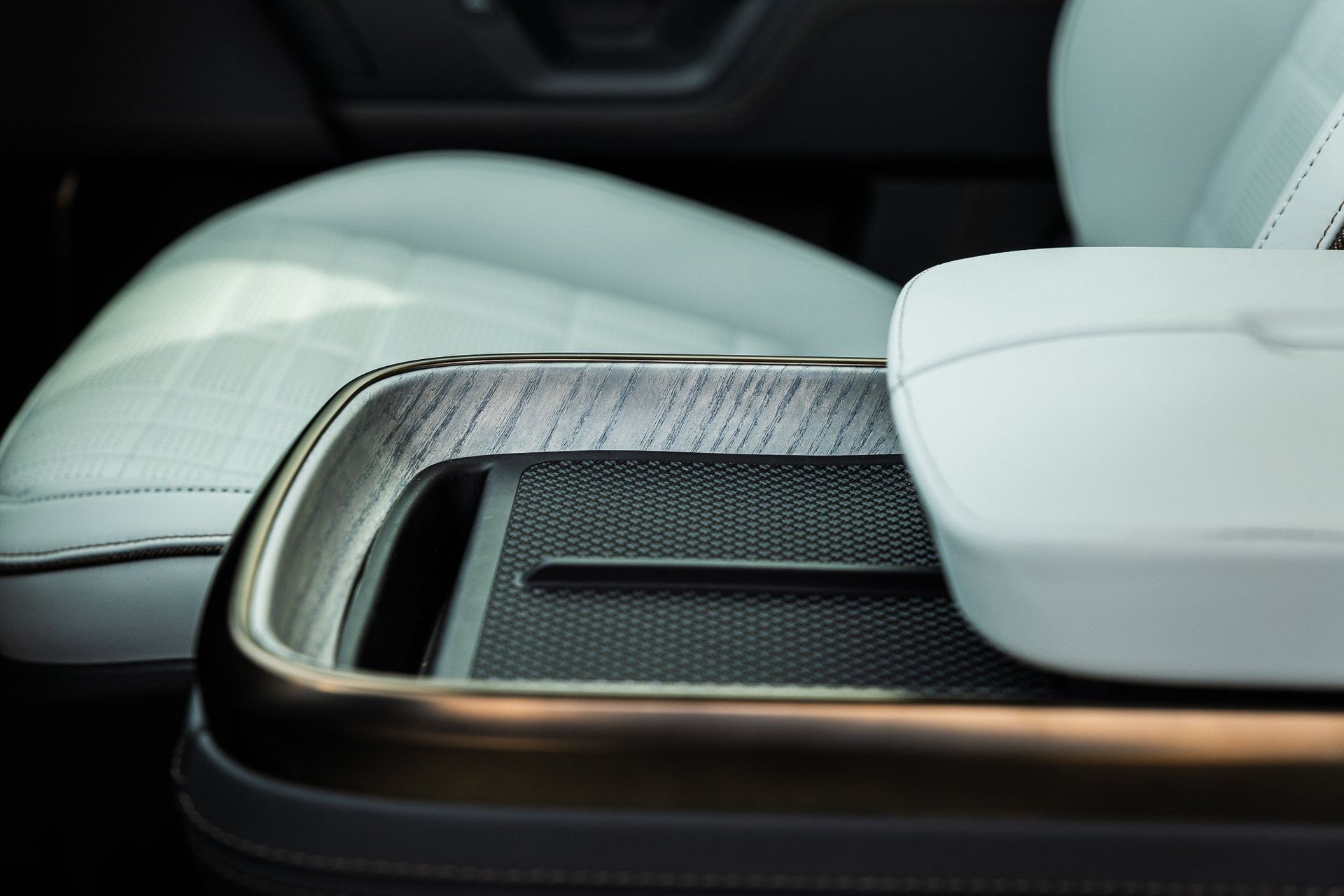 Car center console with a glossy wood-trimmed storage compartment and white leather seats