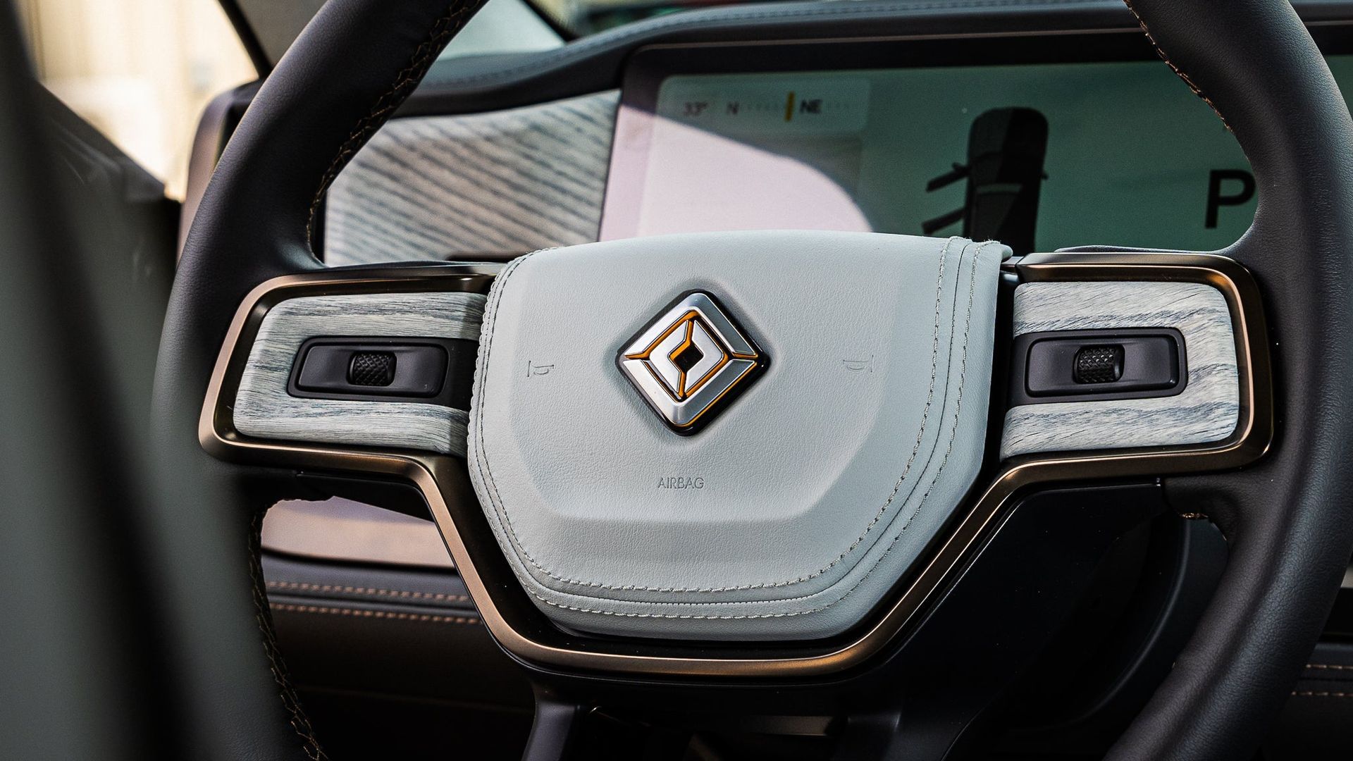 Close-up of a luxury car steering wheel with a diamond-shaped logo and digital display behind it