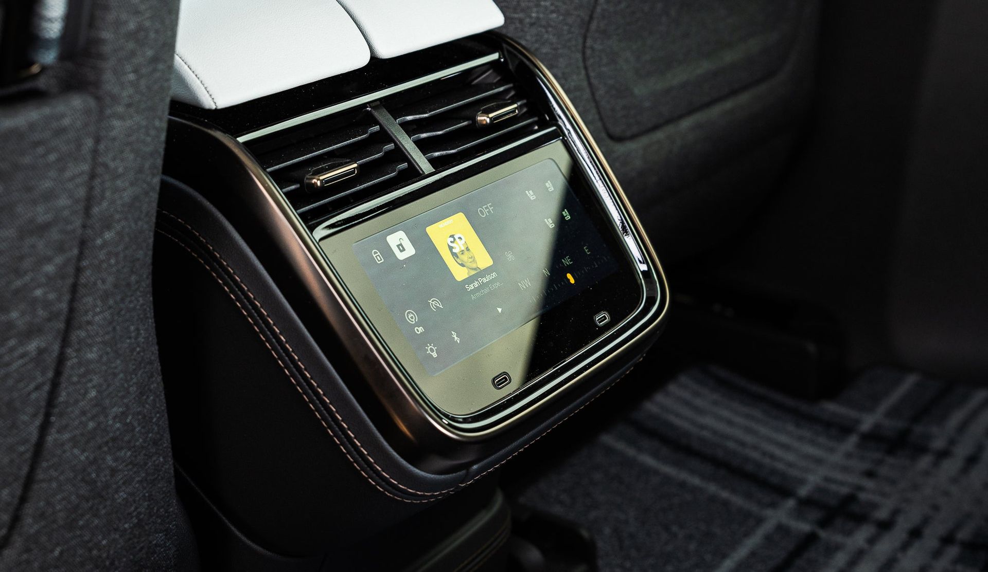Car headrest-mounted entertainment screen in a car interior, showing a video on a reflective display.