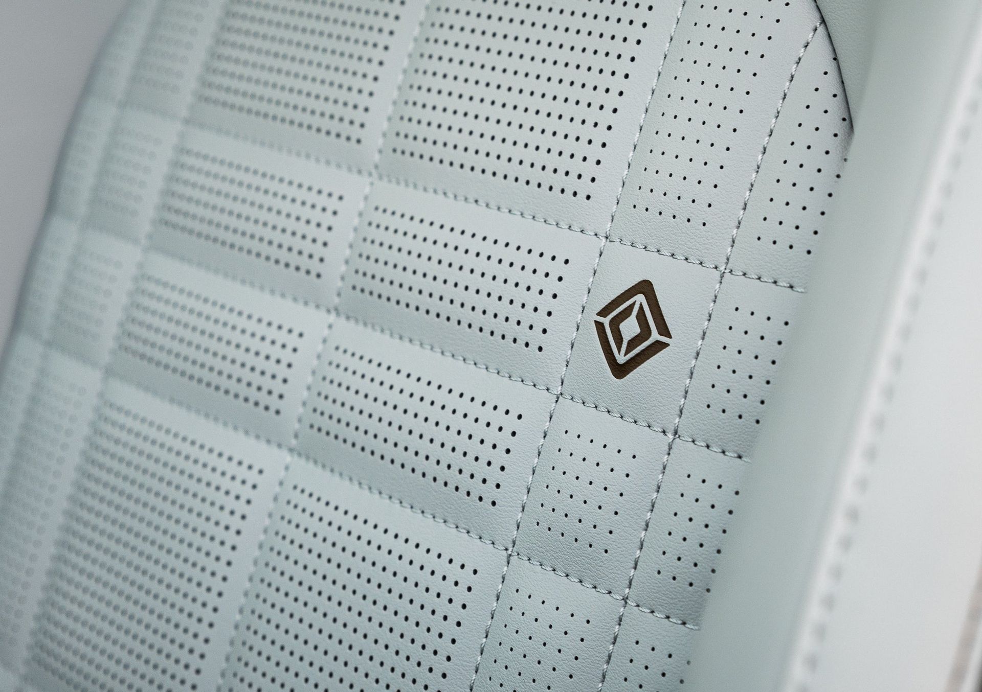Close-up of a light gray perforated car seat with a small black logo badge