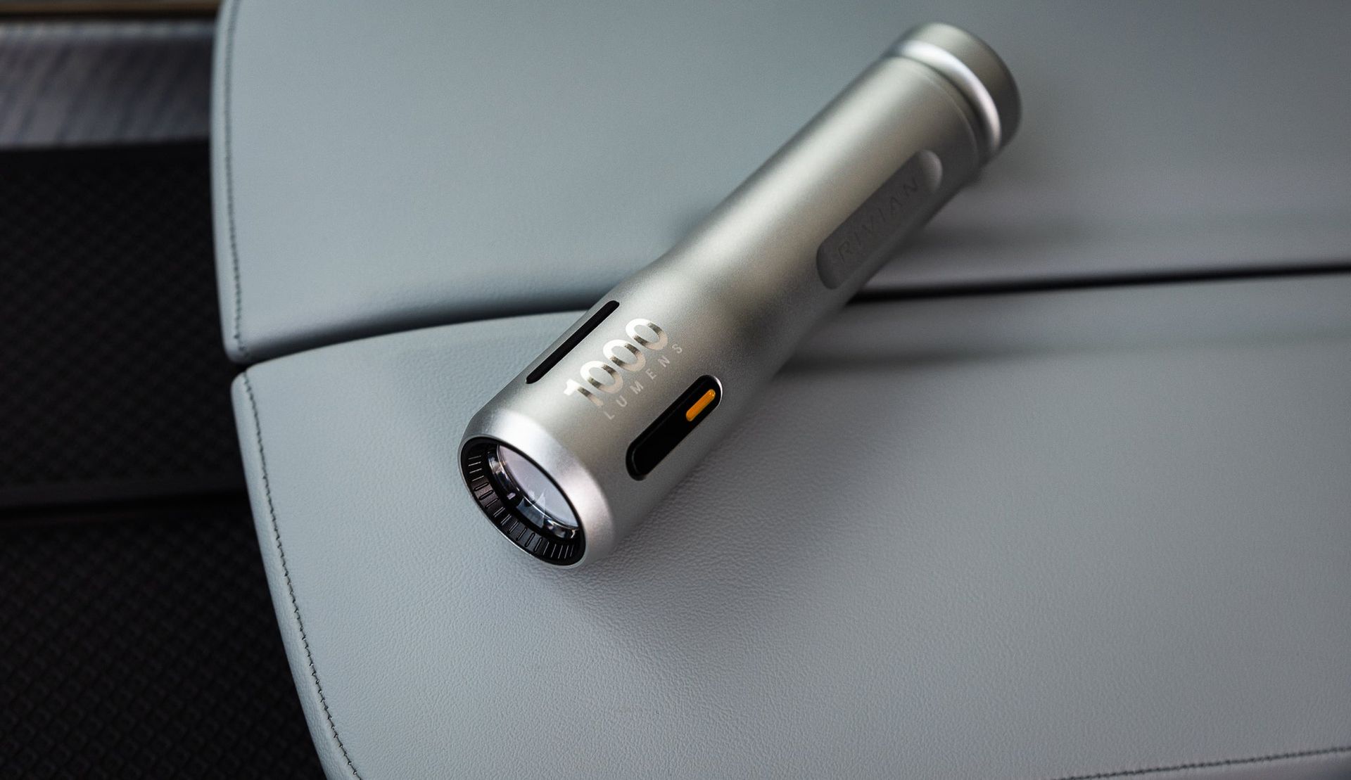 Silver cylindrical flashlight lying on a gray car seat