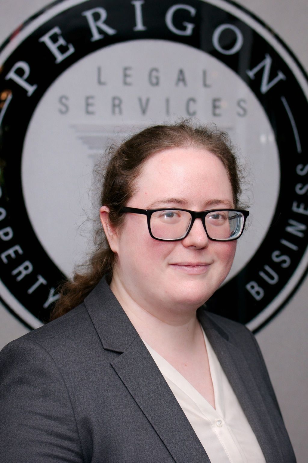 Smiling person in glasses and gray blazer in front of Perigon Legal Services sign
