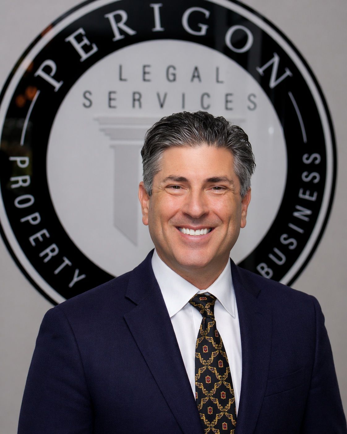 Man in navy suit smiling in front of a Perrigon Legal Services sign