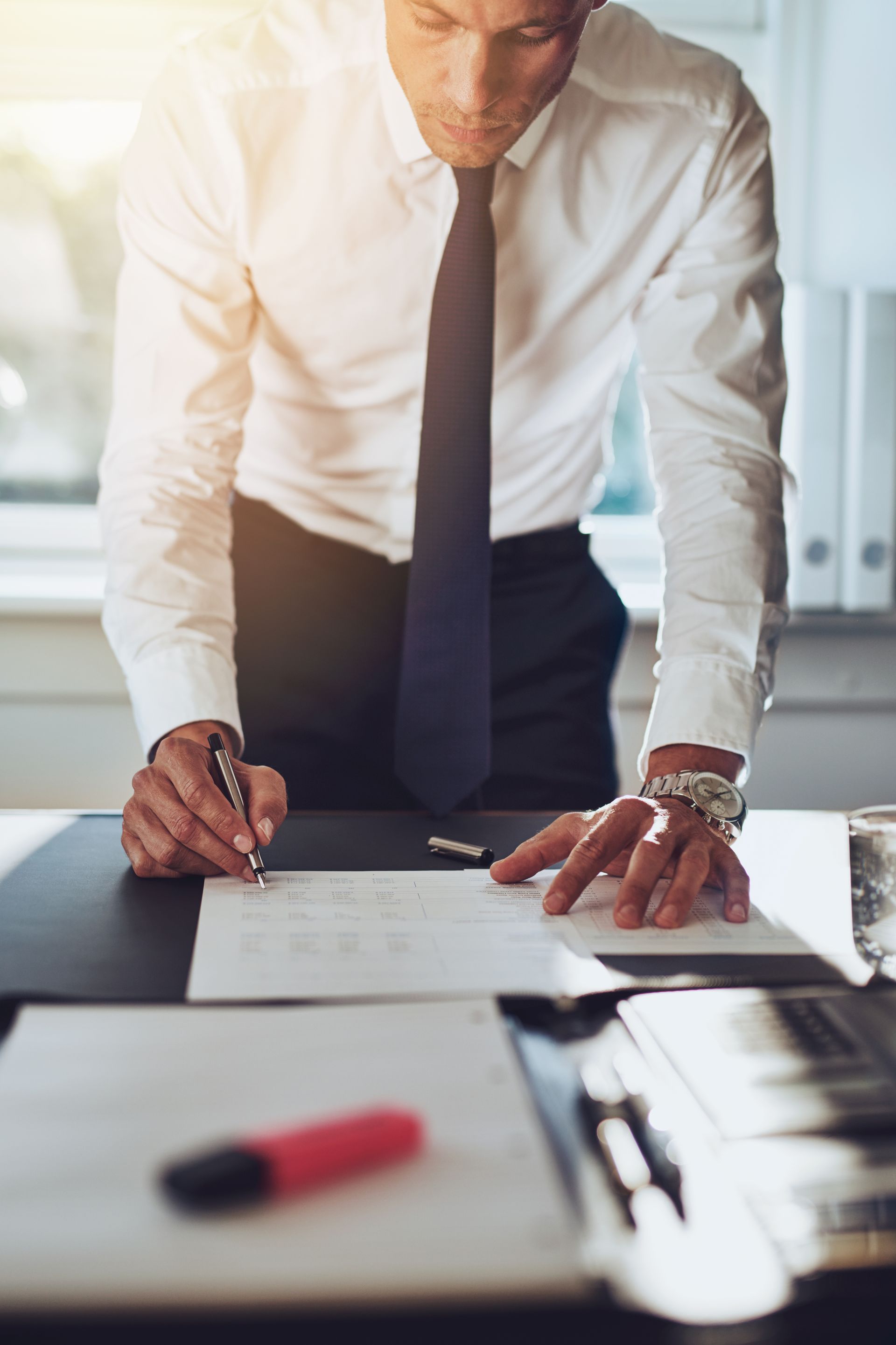 Man in white shirt and tie signing a document at an office desk