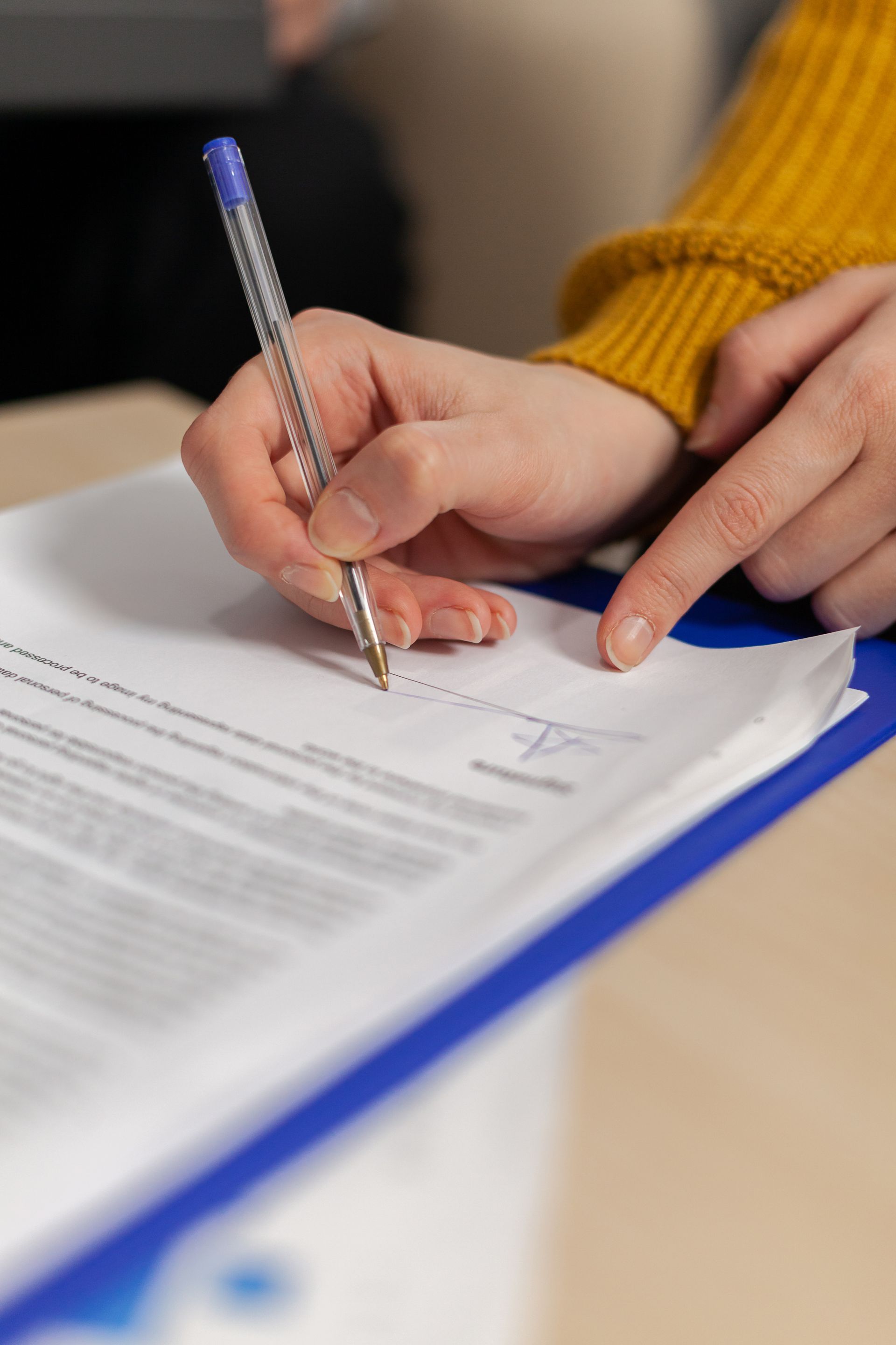Hands filling out a form on a clipboard with a blue pen