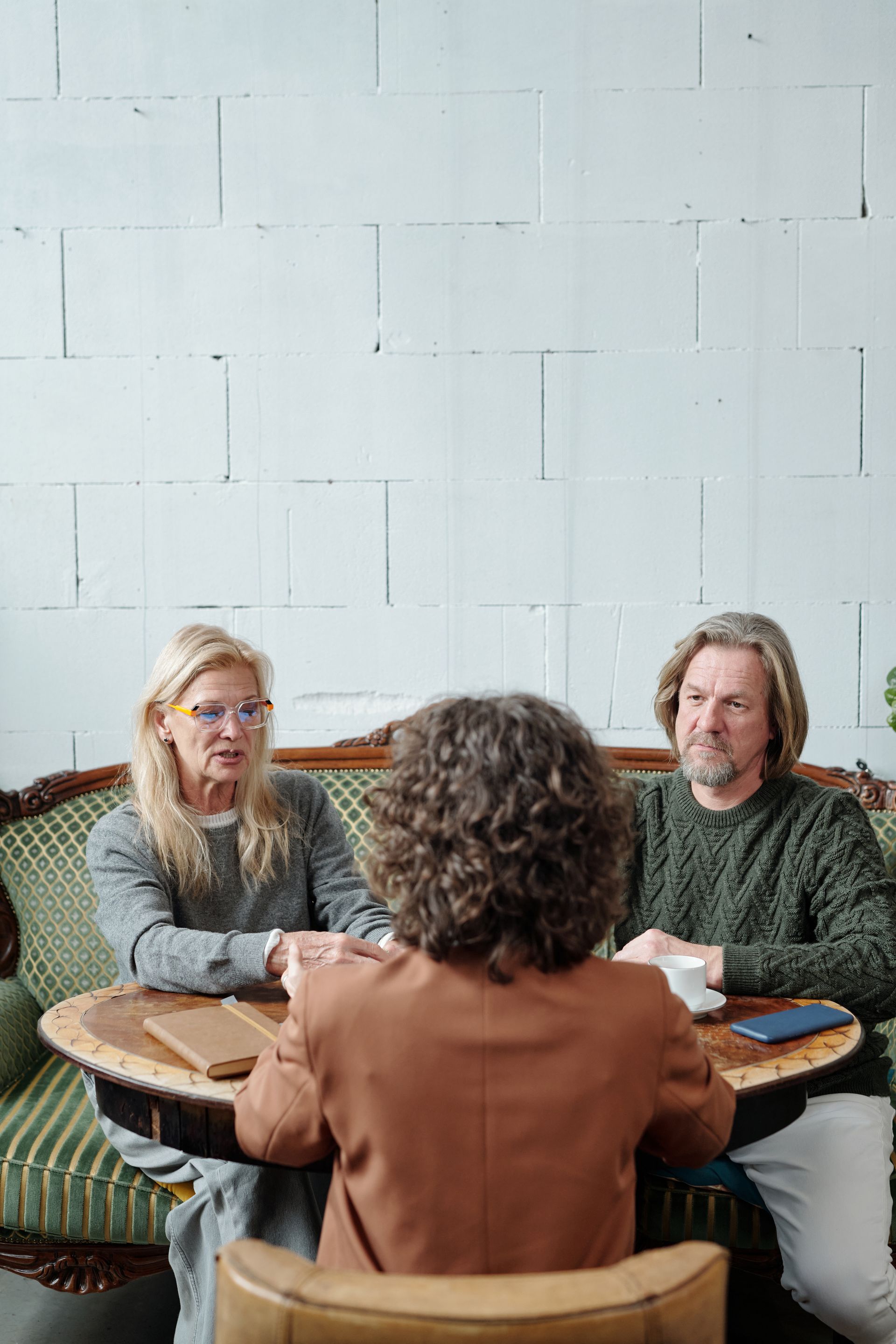 Three people sit around a small round table in a bright room, talking over drinks.