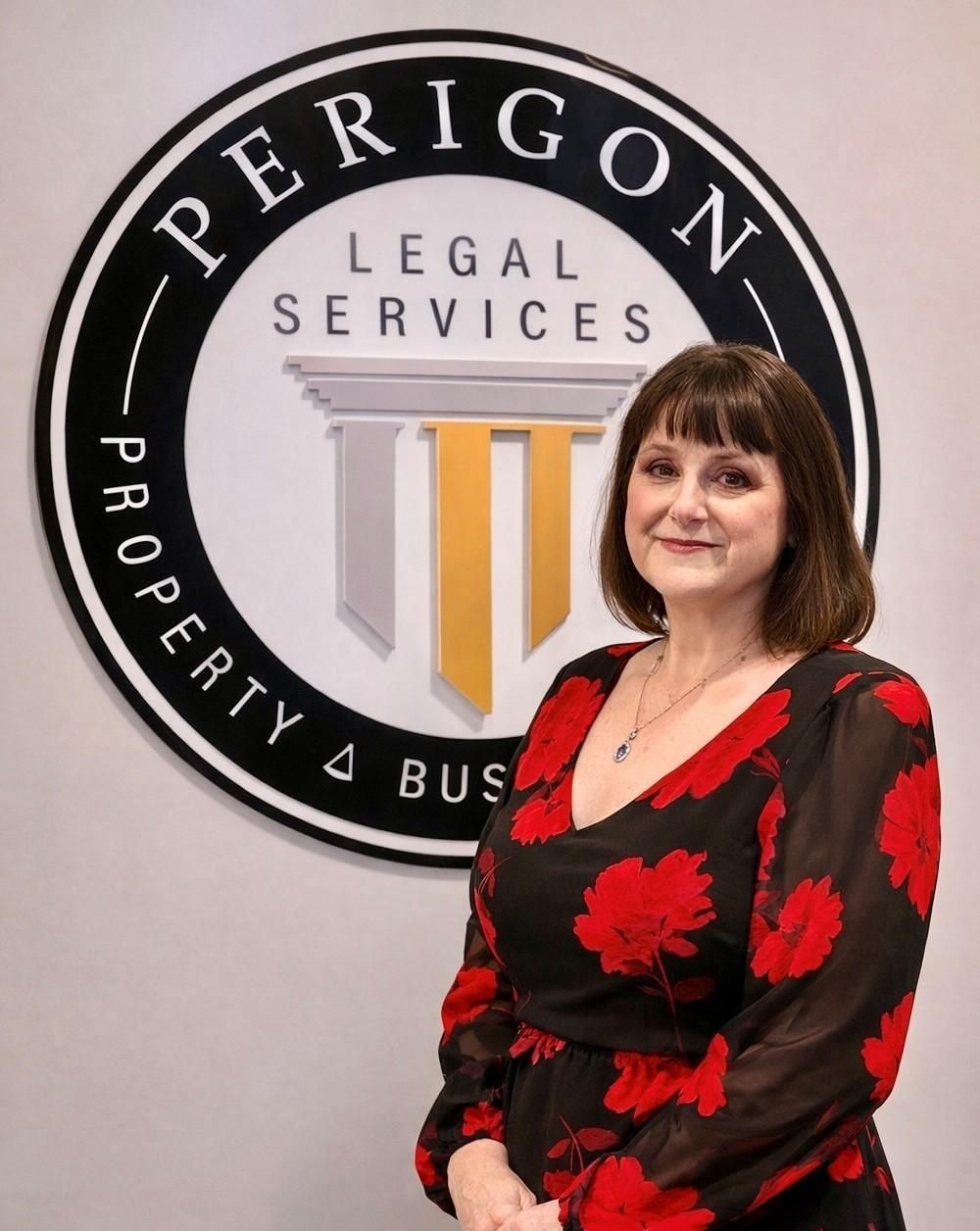 Woman standing in front of Perigon Legal Services sign, wearing a black dress with red floral pattern.