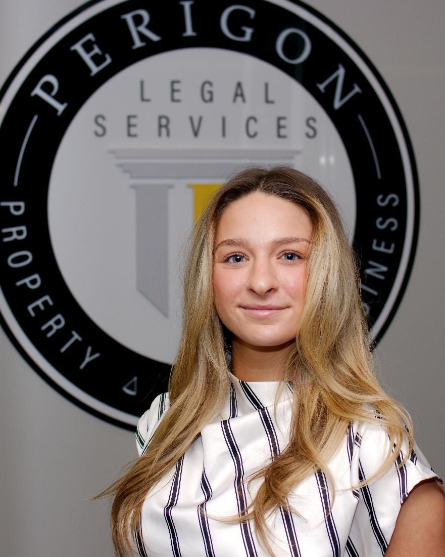 Woman standing before a Perigon Legal Services sign, wearing a white striped shirt and smiling gently