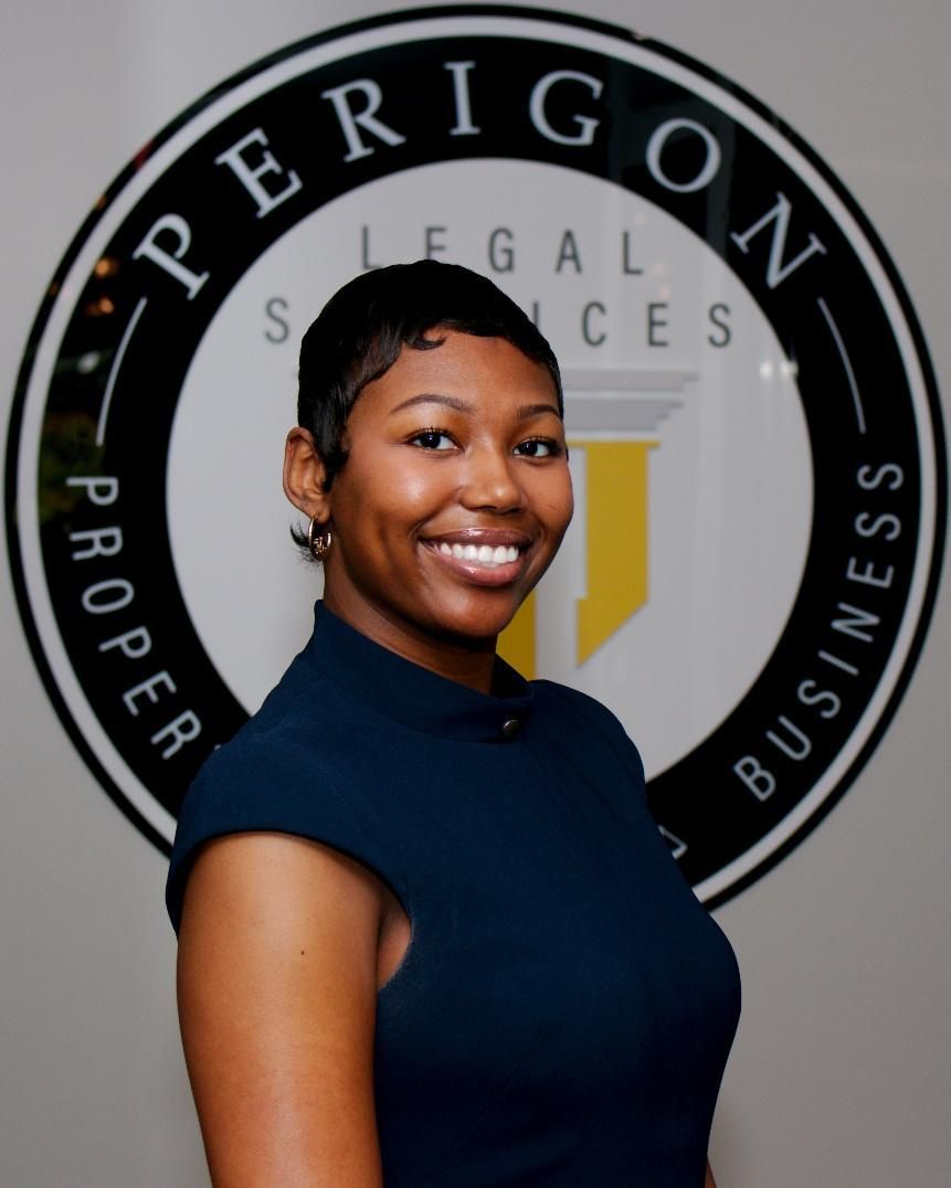 Smiling person in a navy shirt standing in front of a Perigon Legal Services sign