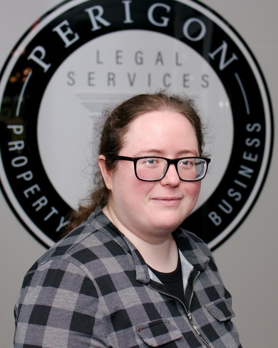 Portrait of a person in glasses and plaid shirt in front of a Perrigon Legal Services sign