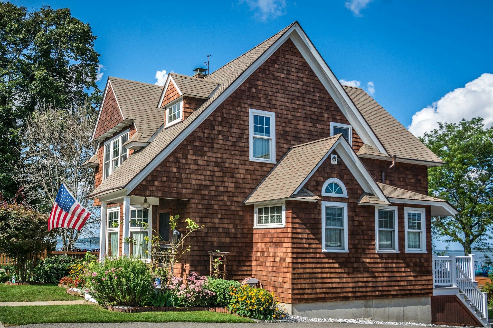 Brick house with a steep roof, American flag, and landscaped yard under a blue sky