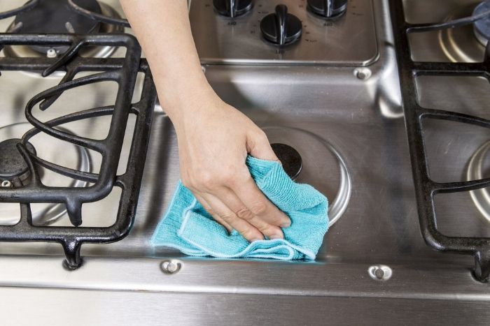 A Person is Cleaning a Stove Top With a Towel — Lease Clean Newcastle in Newcastle, NSW