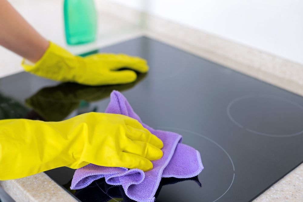 A Person is Cleaning a Stove Top With a Cloth — Lease Clean Newcastle in Warners Bay, NSW