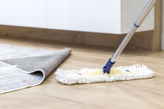 A Mop is Being Used to Clean a Wooden Floor Next to a Rug — Lease Clean Newcastle in Lake Macquarie, NSW