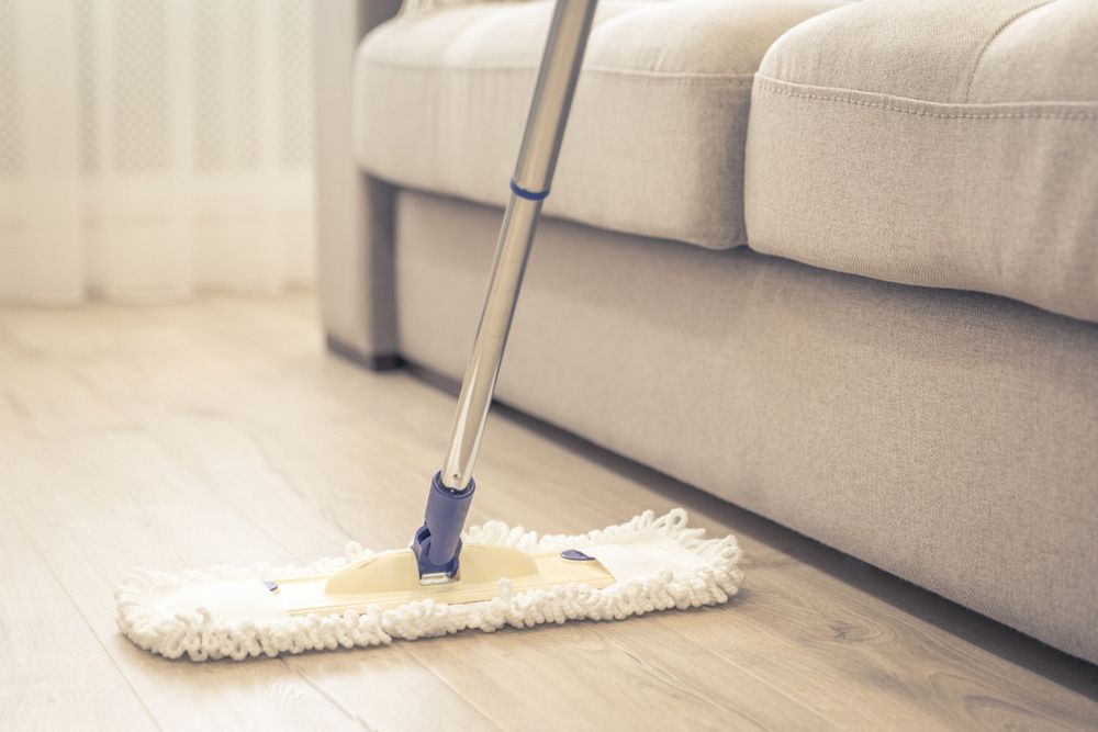 A Mop is Sitting on a Wooden Floor Next to a Couch — Lease Clean Newcastle in Newcastle, NSW
