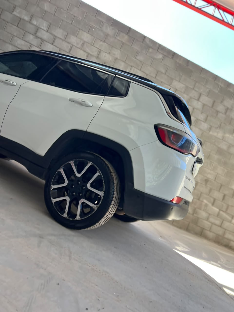 SUV blanco estacionado en el interior junto a una pared de hormigón, vista en ángulo de la parte trasera.