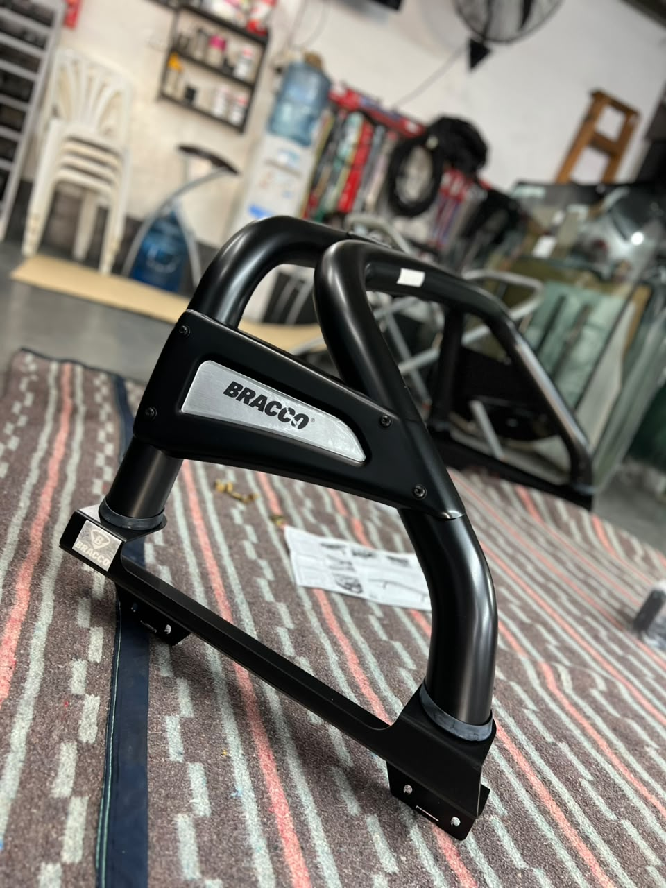 Una barra protectora de metal negro para motocicleta sobre una alfombra a rayas en una habitación que parece un garaje.