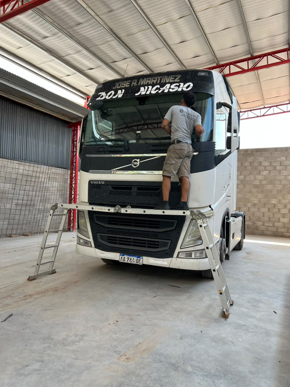 Una persona limpia un camión Volvo blanco dentro de un almacén, subida a una escalera.