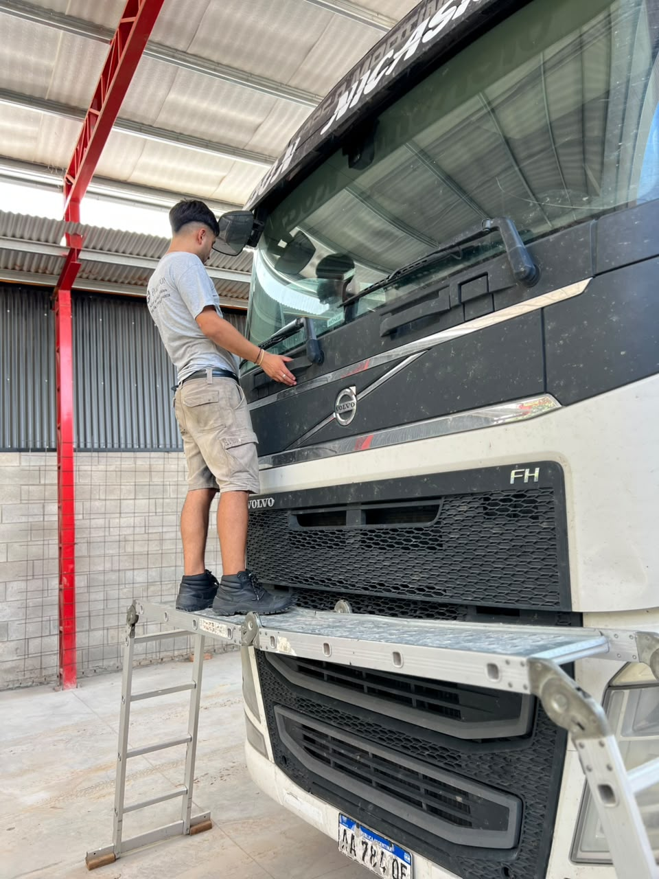 Un trabajador limpia el parabrisas de un camión Volvo negro en un taller mecánico.