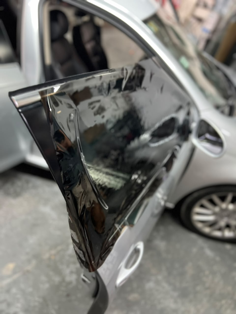 Espejo retrovisor lateral de un coche negro dañado con la carcasa agrietada en un vehículo plateado, vista de cerca.