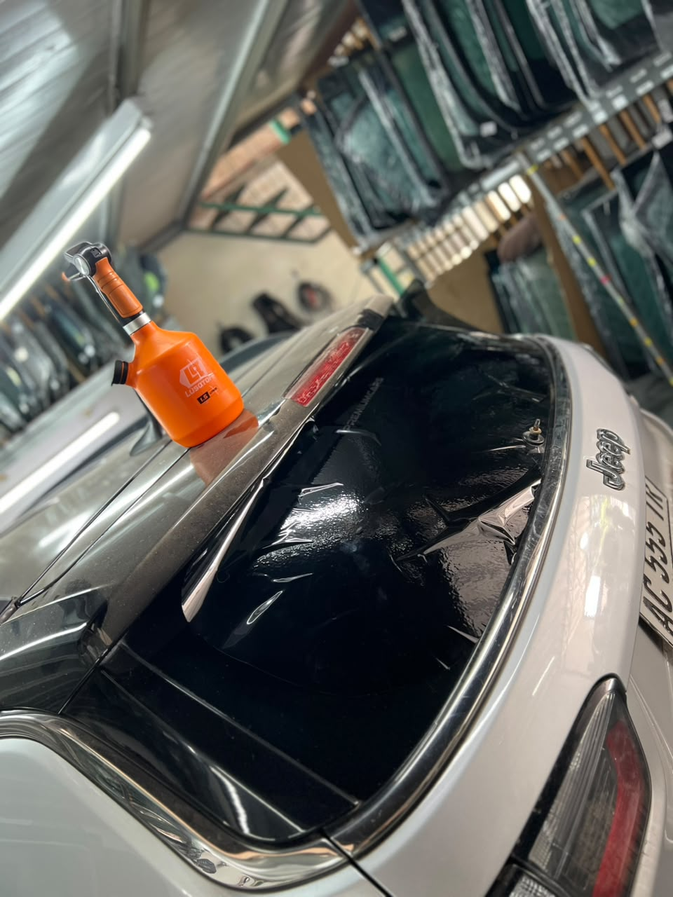 Una botella naranja sobre el techo de un coche en un aparcamiento, con un coche blanco y ventanas oscuras.