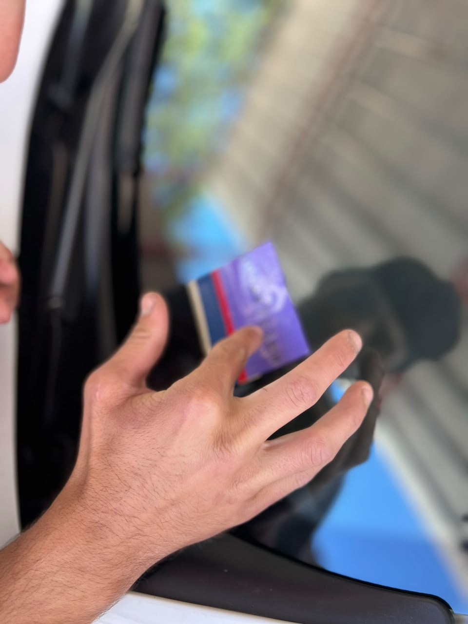 Una mano sostiene una tarjeta de transporte morada cerca de la ventana de un tren mientras se aborda.