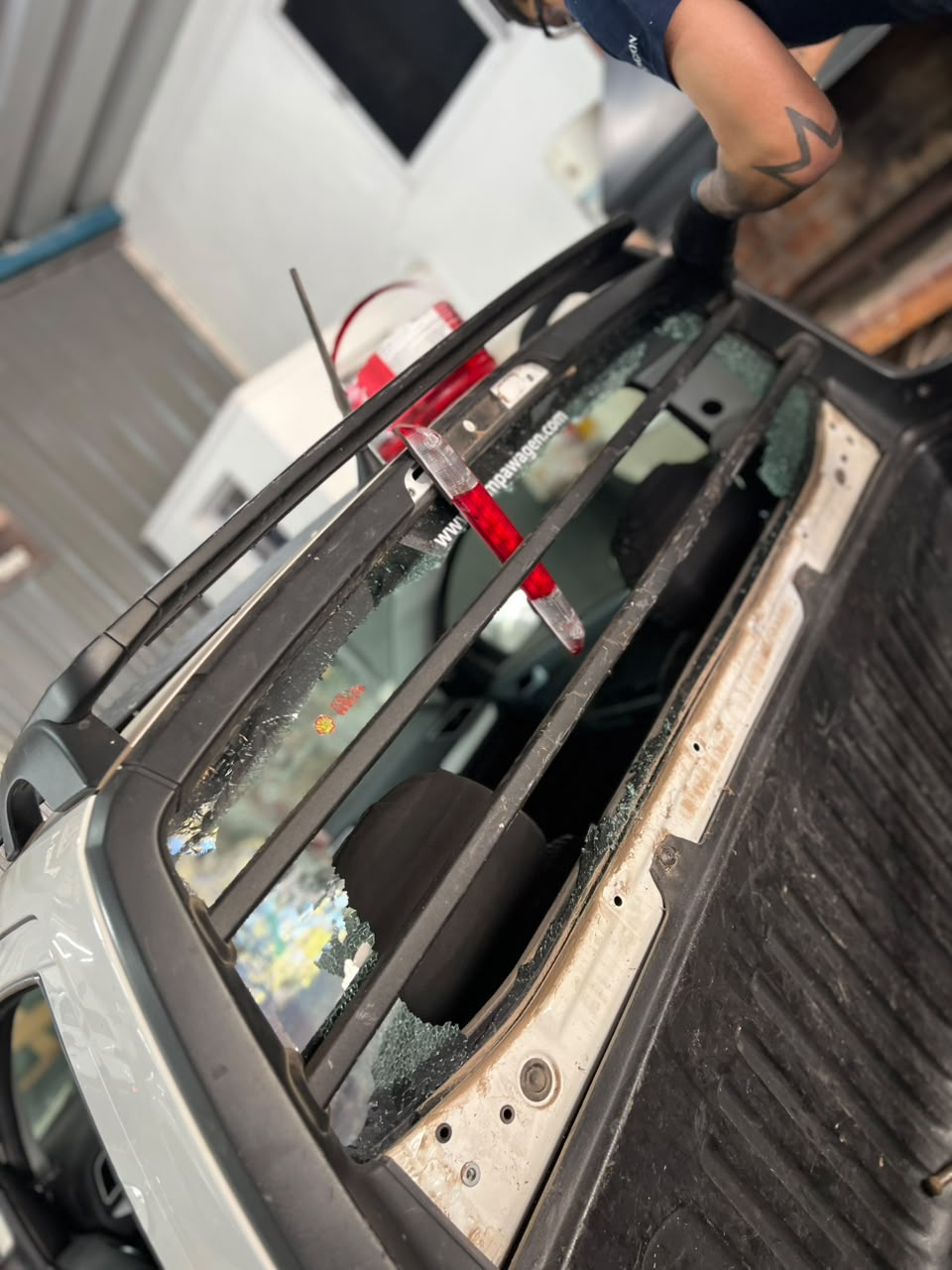 Primer plano de la abertura del techo de un coche dañado, con cristales rotos y la mano de una persona cerca.