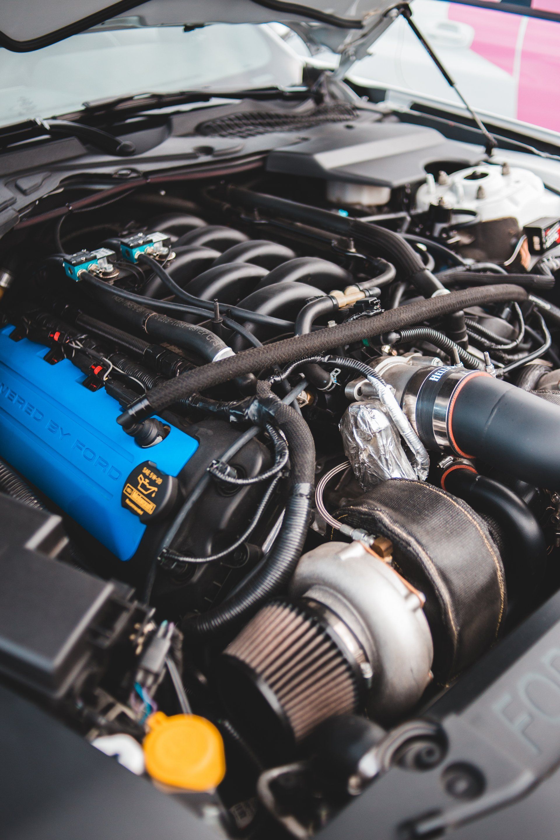 A modified Ford Mustang engine bay featuring a turbocharger with a heat-wrapped housing, blue valve covers, and an intake.
