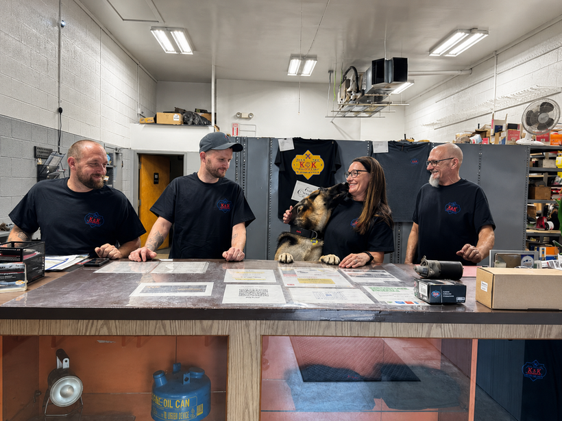 Four people stand behind a workbench in a bright workshop, looking at plans and tools.