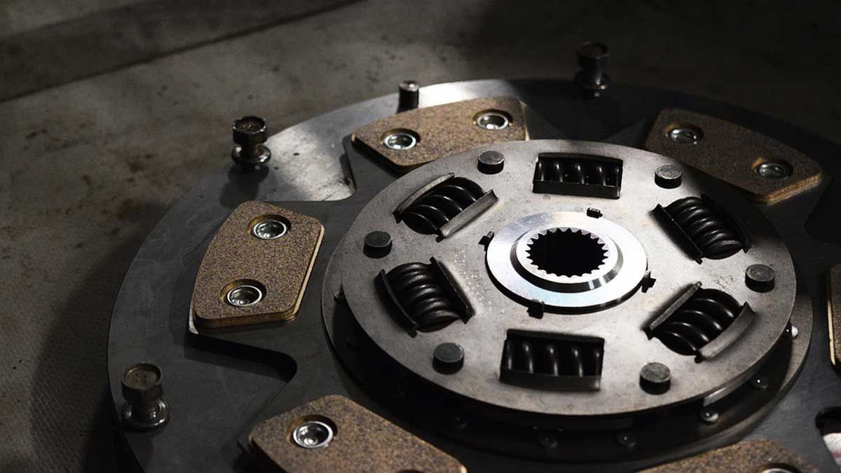 A close-up view of a metallic vehicle clutch disc featuring circular springs and friction pads on a dark background.