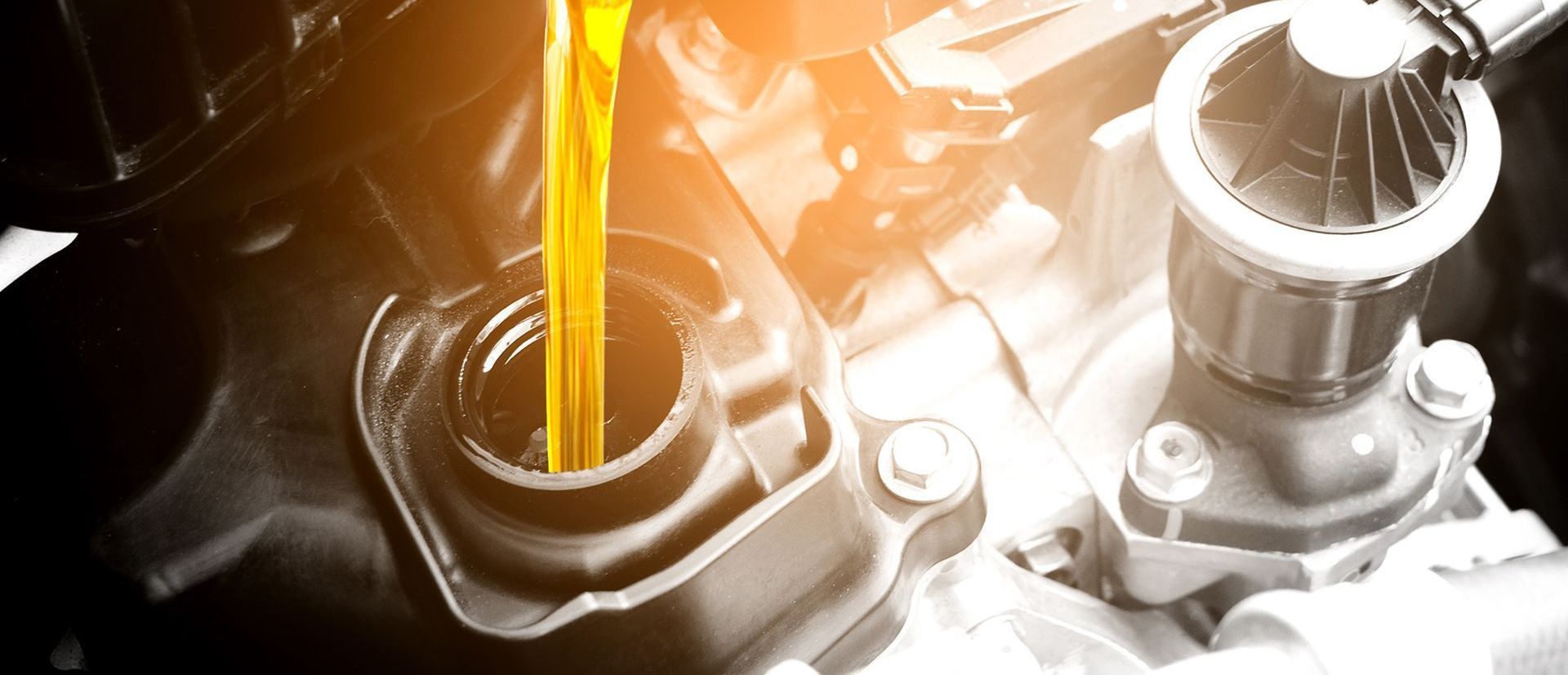 Golden motor oil pouring into a black engine oil filler port.