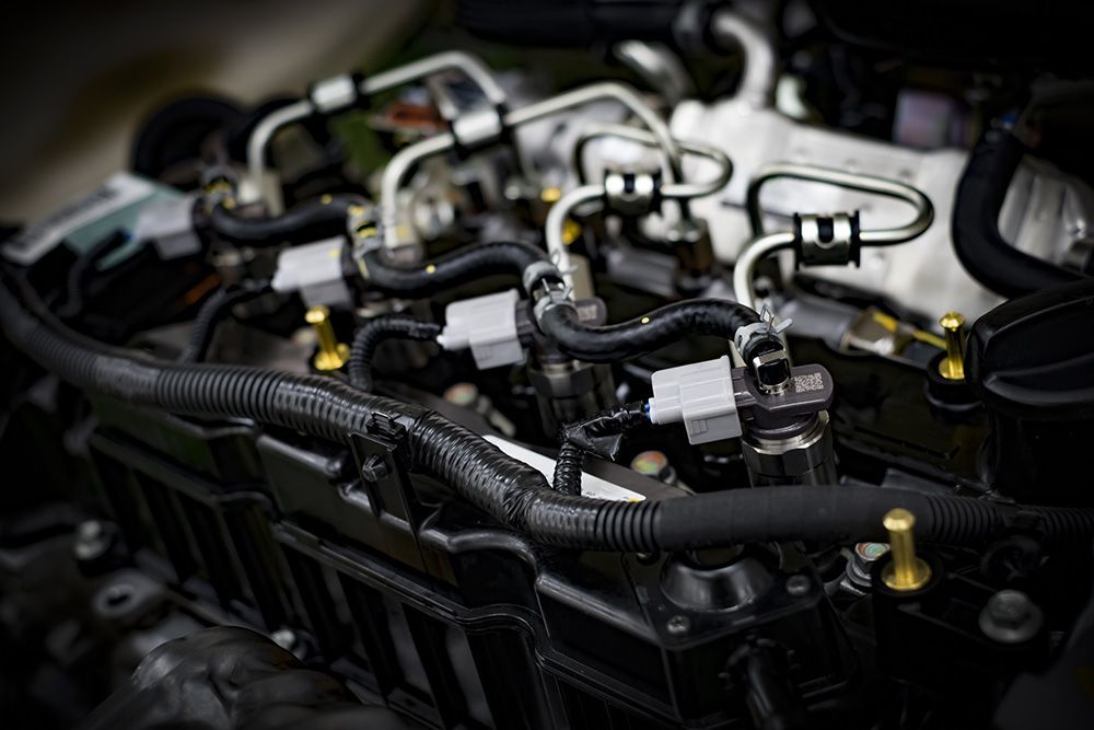 A close-up view of a car engine featuring metal fuel lines, black plastic covers, and electrical wiring components.