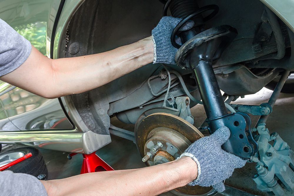 A person wearing gloves replaces the shock absorber on a car raised by a jack stand.