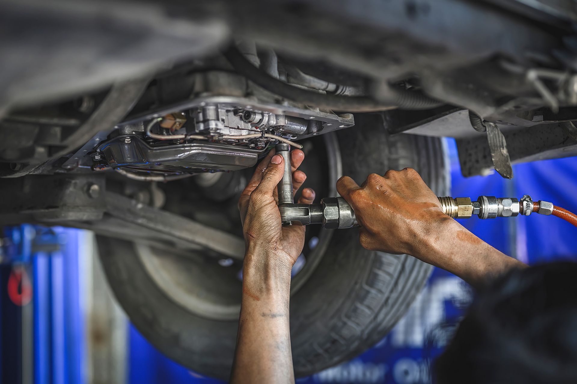 A mechanic uses a pneumatic tool to work on the underside of a vehicle in an auto repair shop.