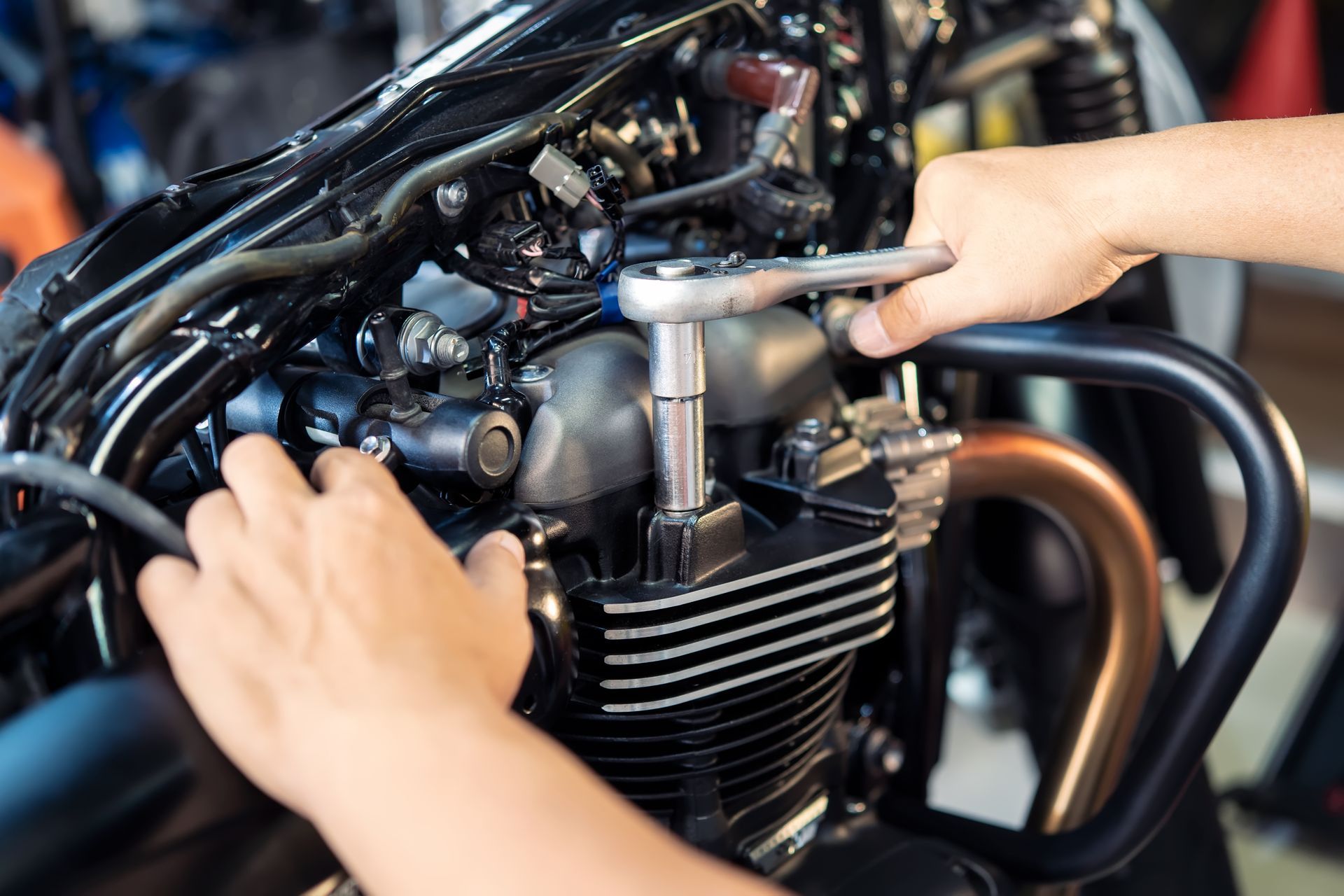 A hand in a white work glove holds an adjustable wrench over the open engine bay of a car, illuminated by sunlight.