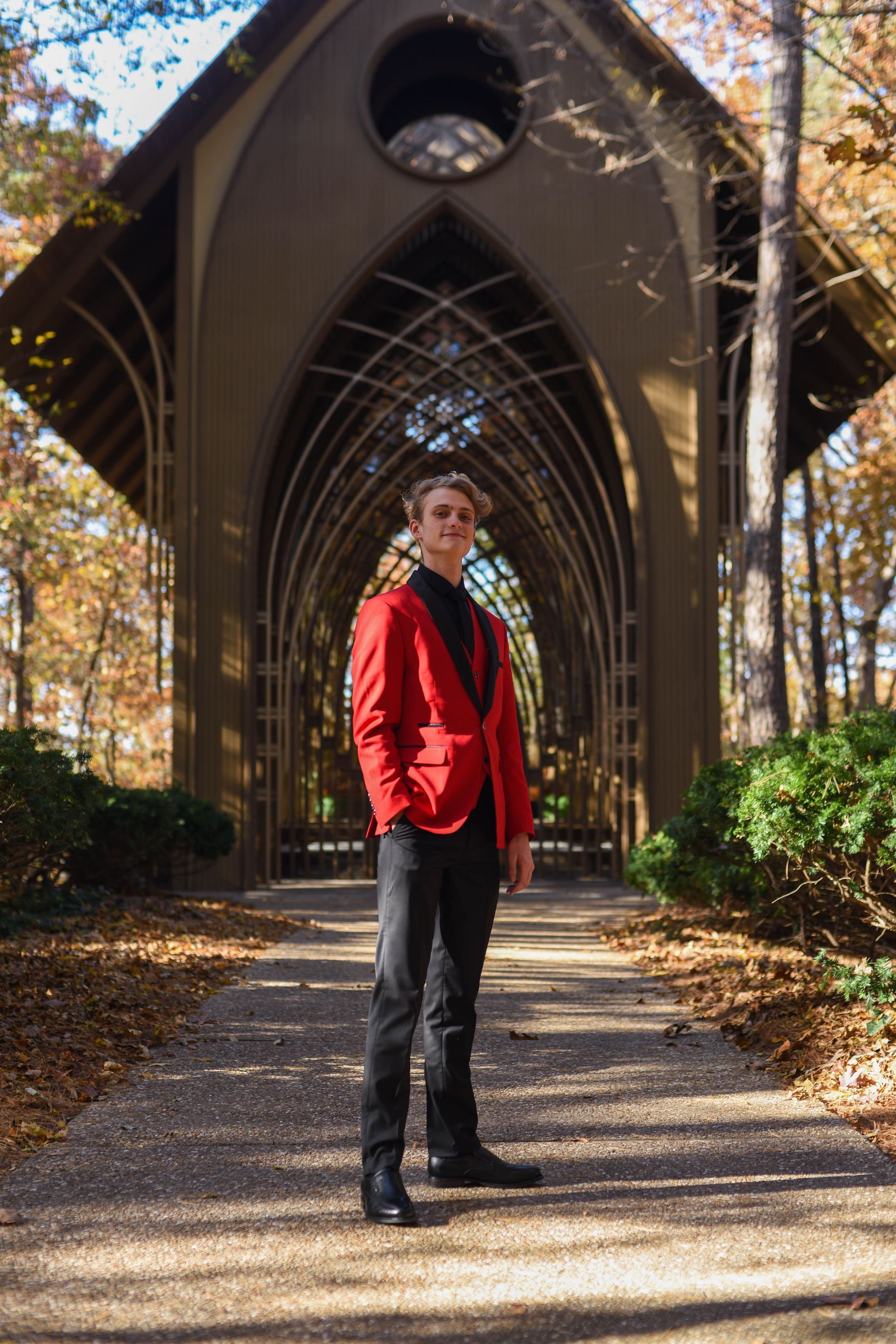 Person in red jacket standing on a path before a gothic archway in a wooded setting