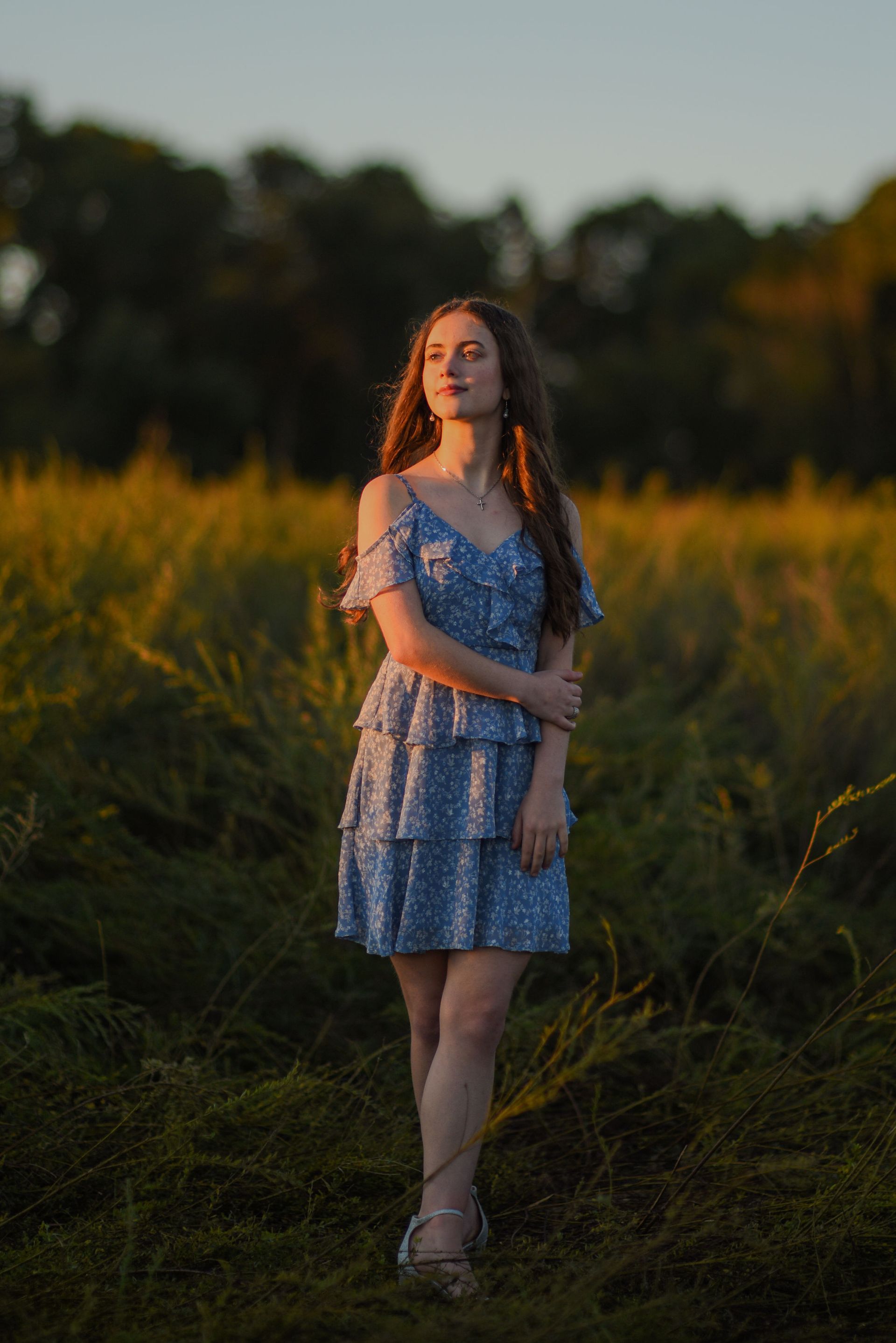 Woman in a blue dress standing in a grassy field at sunset with warm golden light