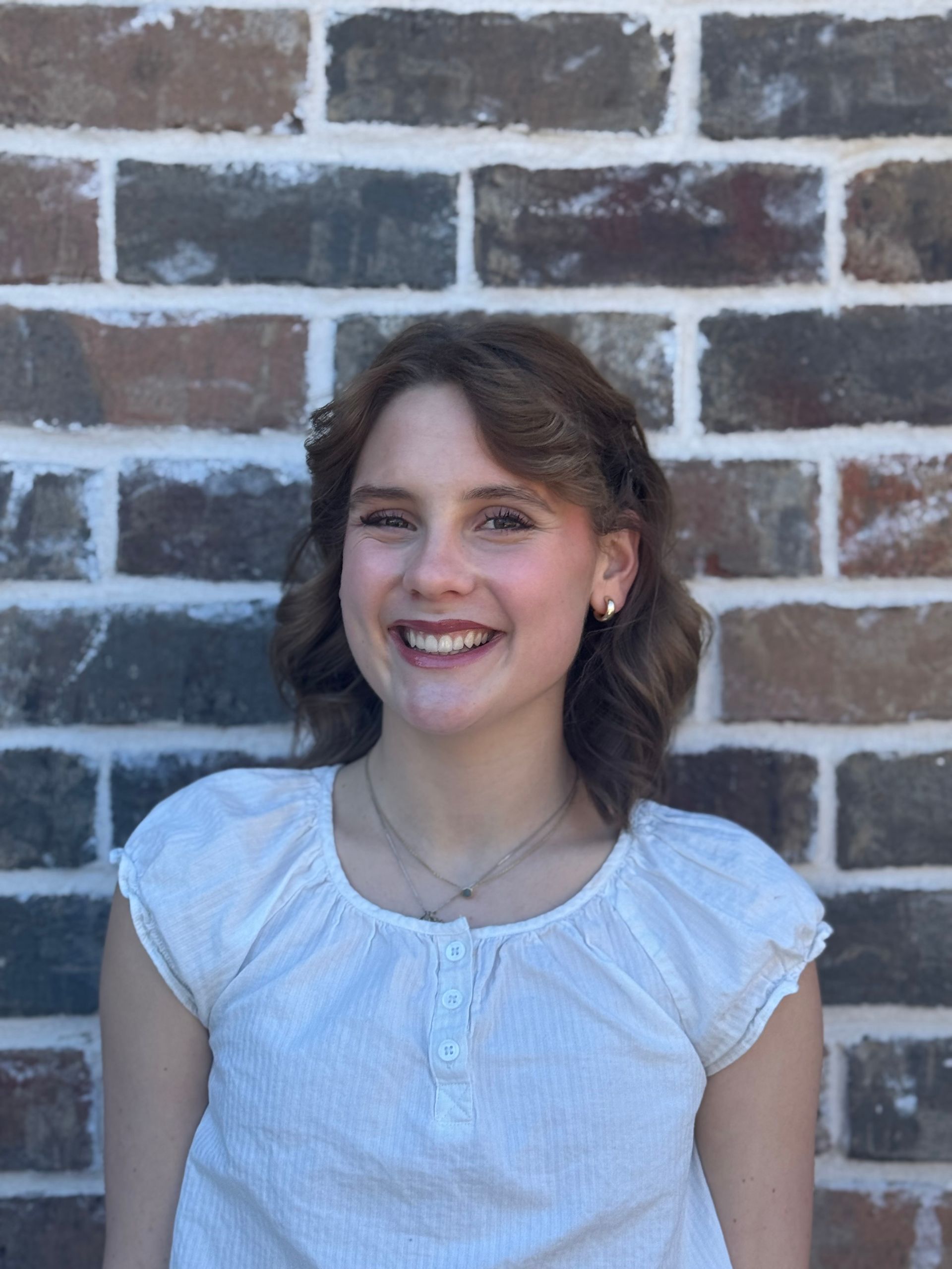 Smiling person in a white blouse standing in front of a brick wall