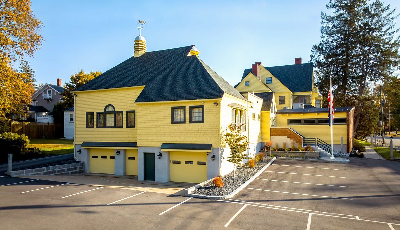 A large yellow house with a black roof is sitting in a parking lot.