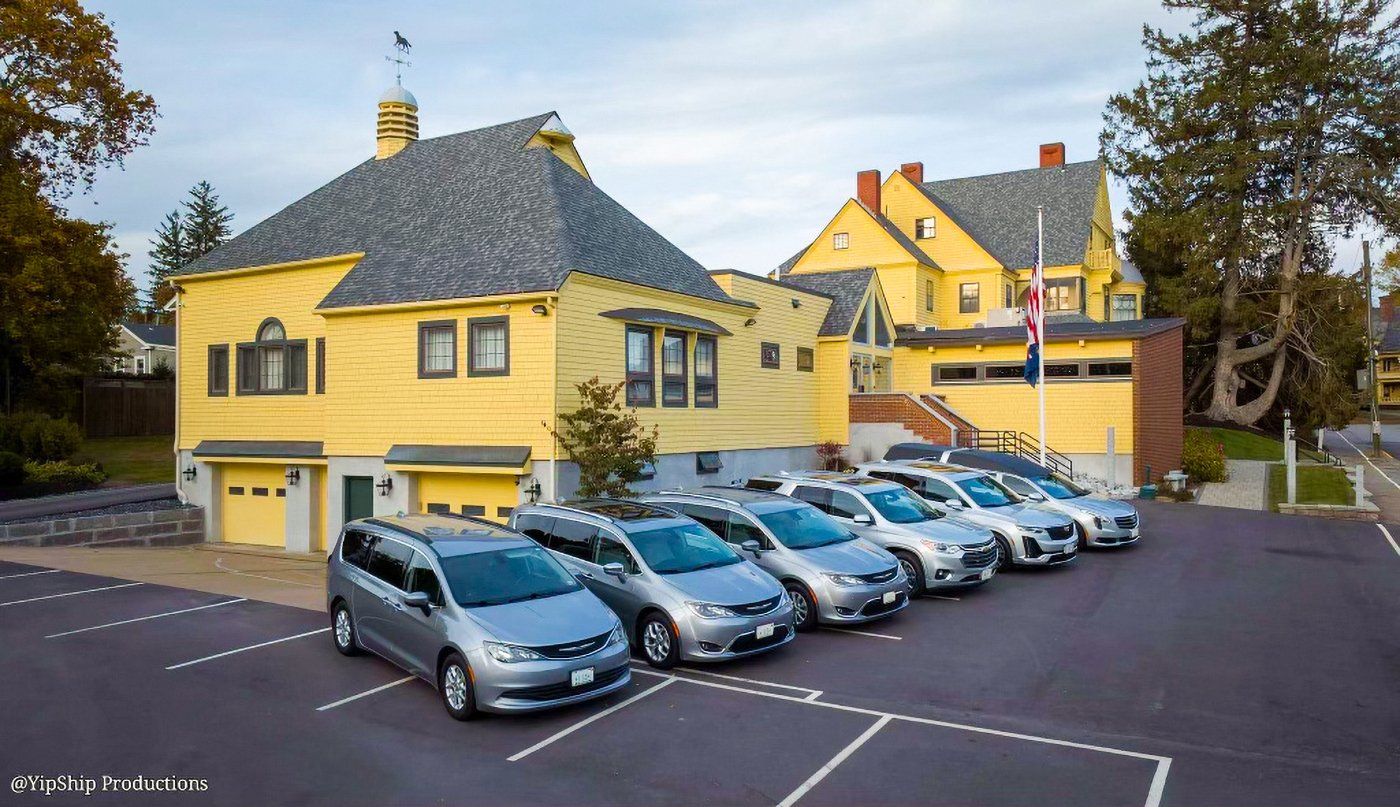 A row of cars are parked in front of a yellow house.
