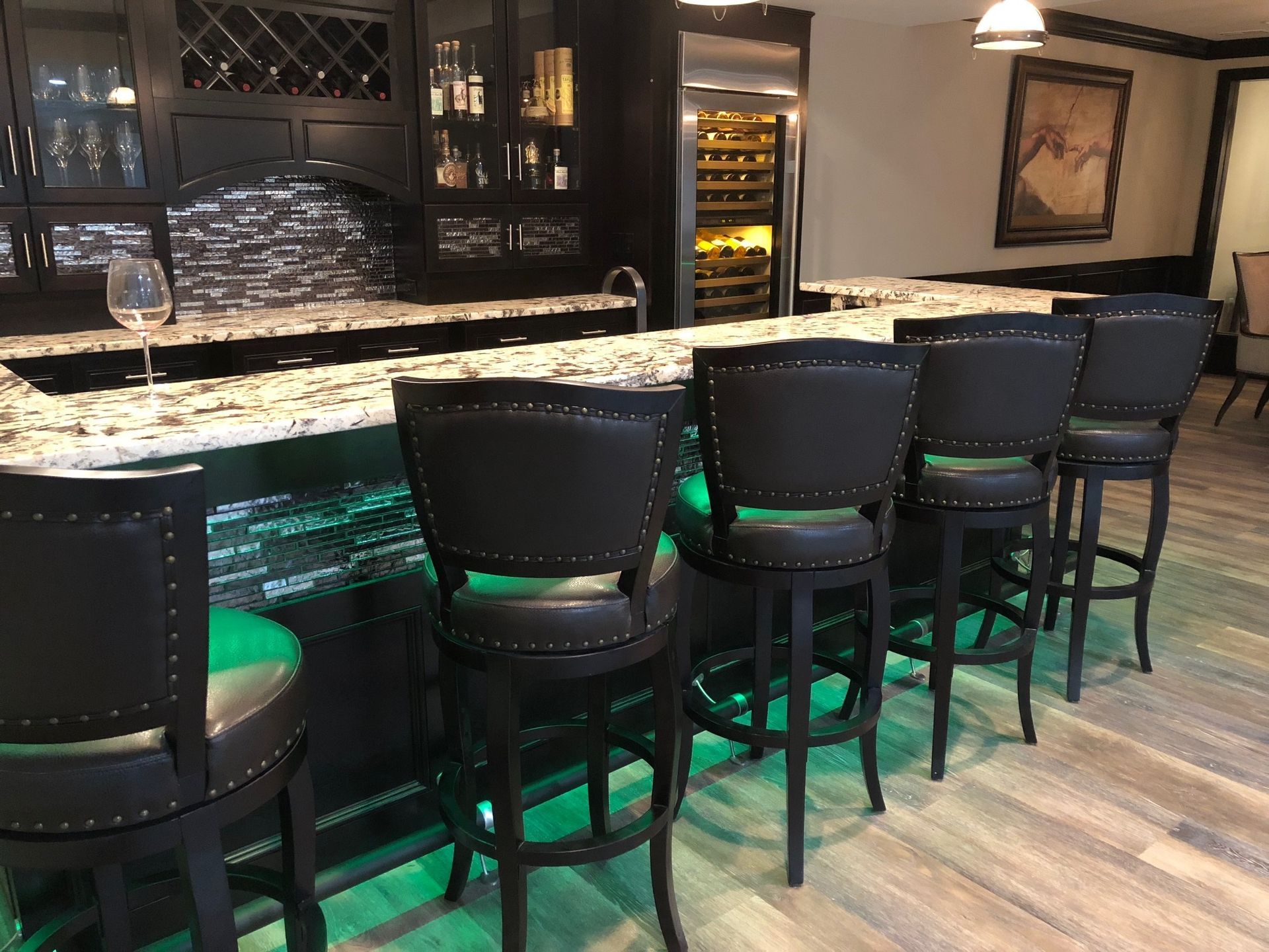 A row of bar stools are lined up in front of a bar with green lights.